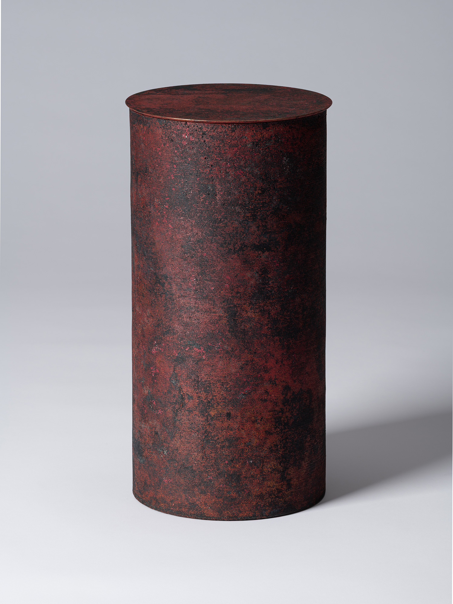 A tall, minimalist cylindrical bronze vessel with a flat, circular lid by Japanese metal artist...