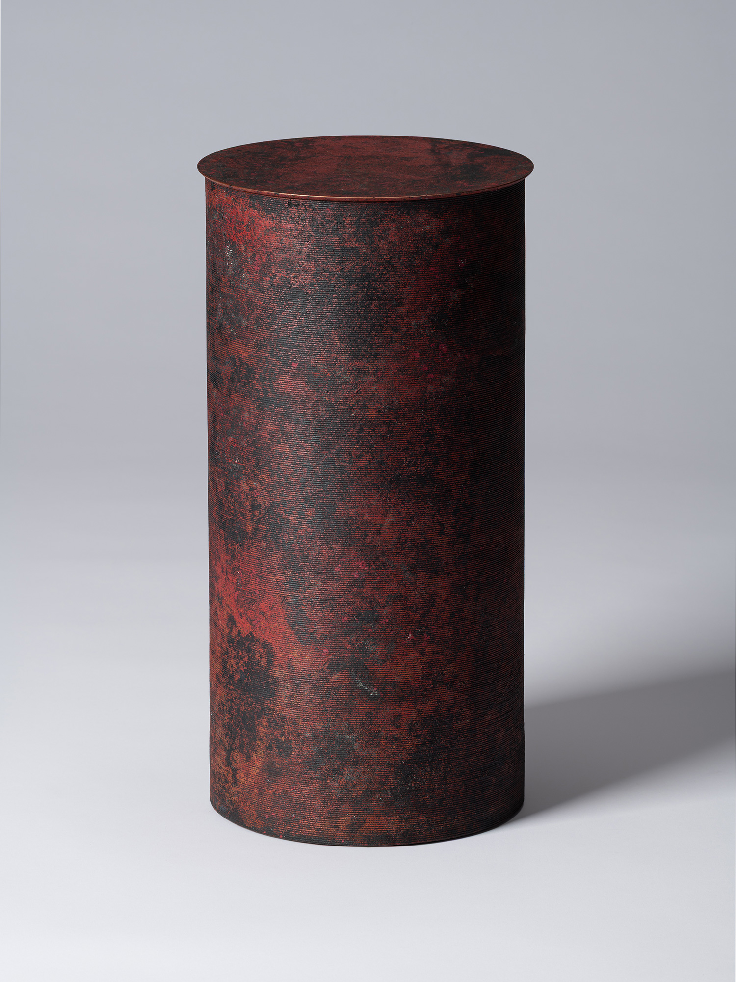 A tall, minimalist cylindrical bronze vessel with a flat, circular lid by Japanese metal artist...