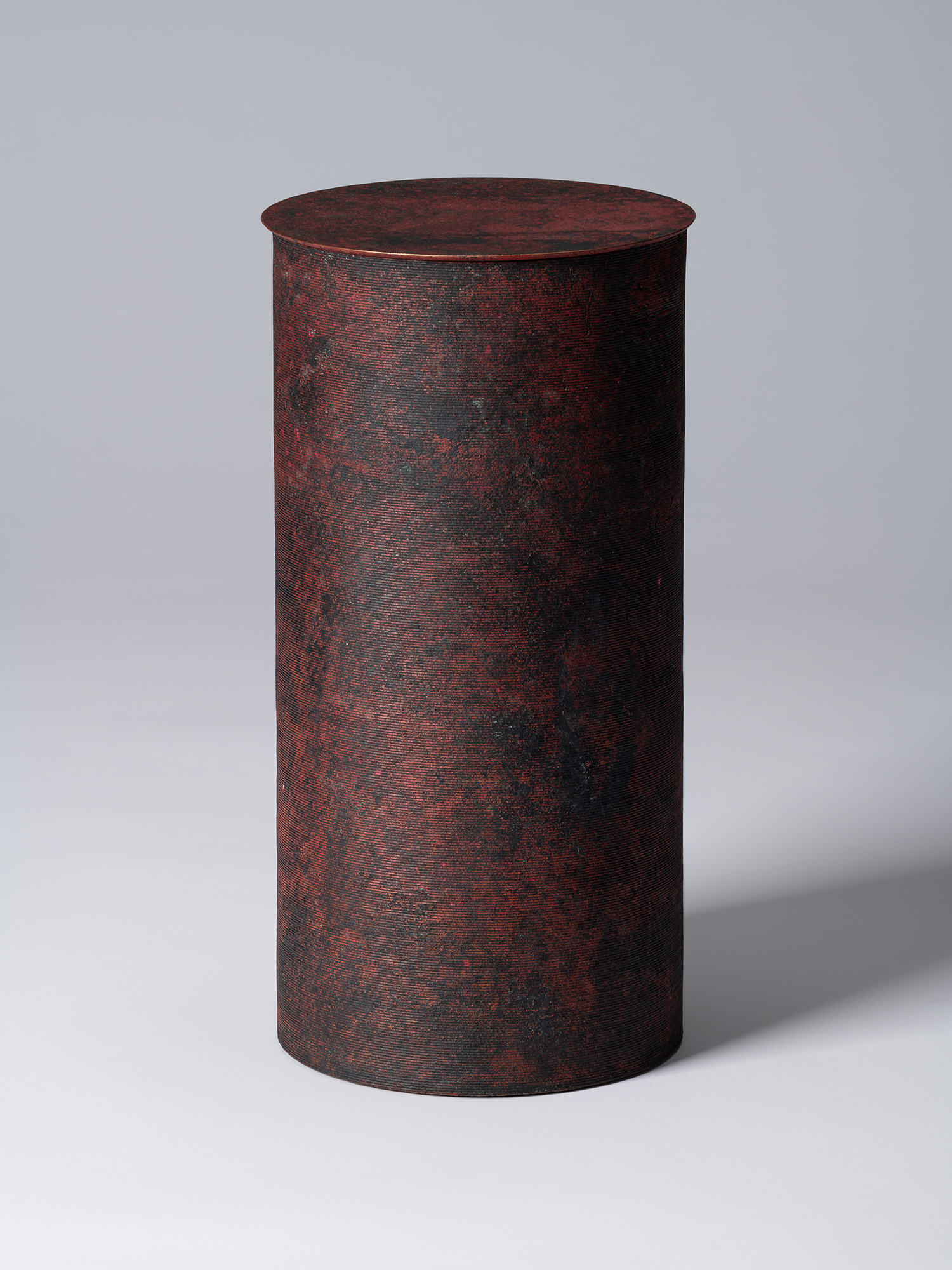 A tall, minimalist cylindrical bronze vessel with a flat, circular lid by Japanese metal artist...