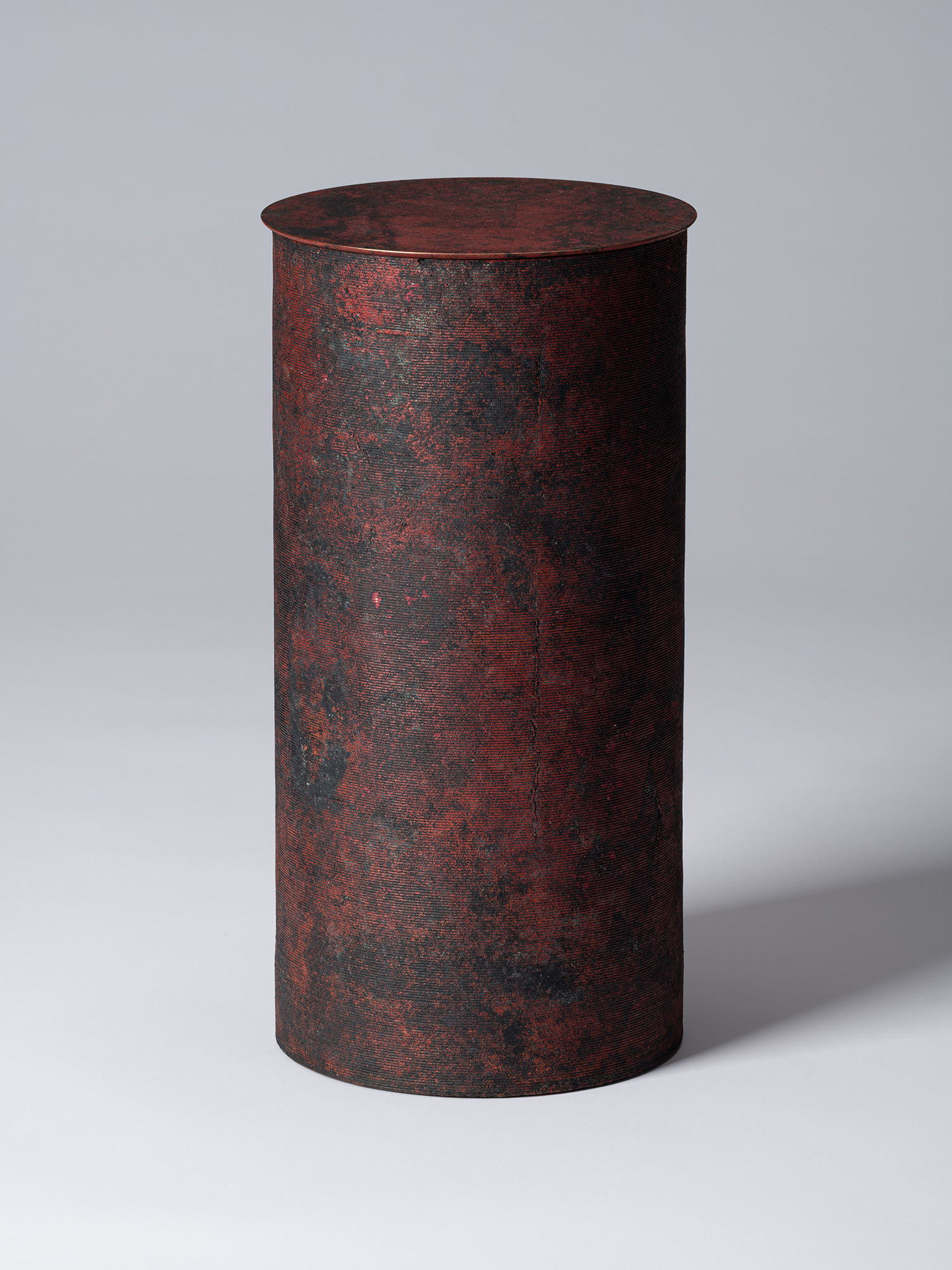 A tall, minimalist cylindrical bronze vessel with a flat, circular lid by Japanese metal artist...