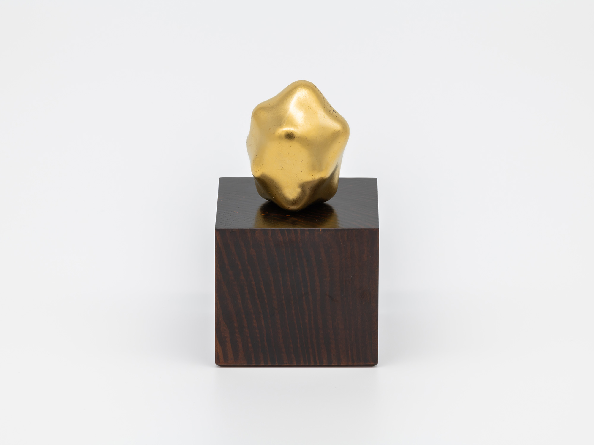 Untitled by Genta Ishizuka displayed with its accompanying wooden pedestal. A small, irregularly...