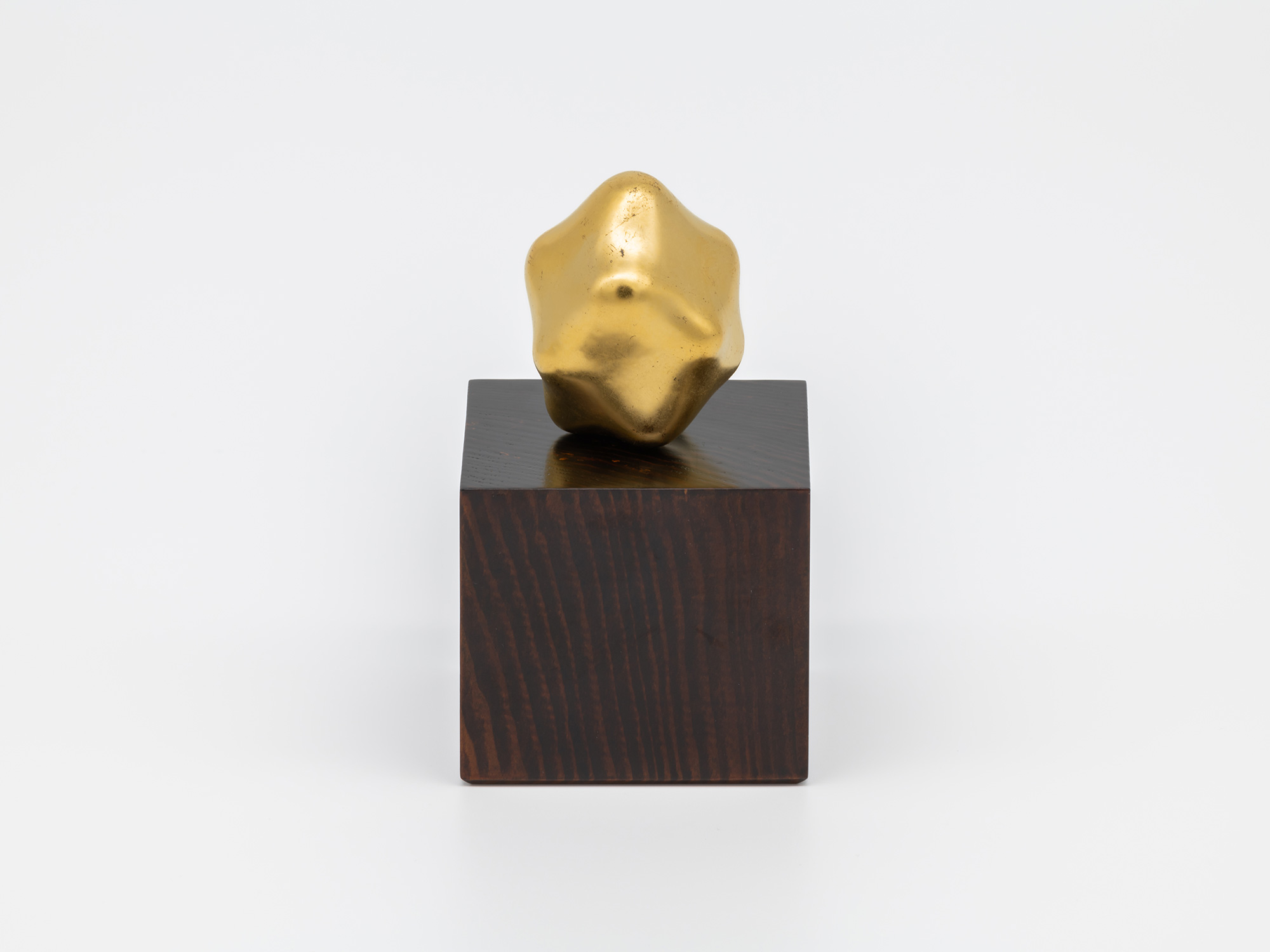 Untitled by Genta Ishizuka displayed with its accompanying wooden pedestal. A small, irregularly...