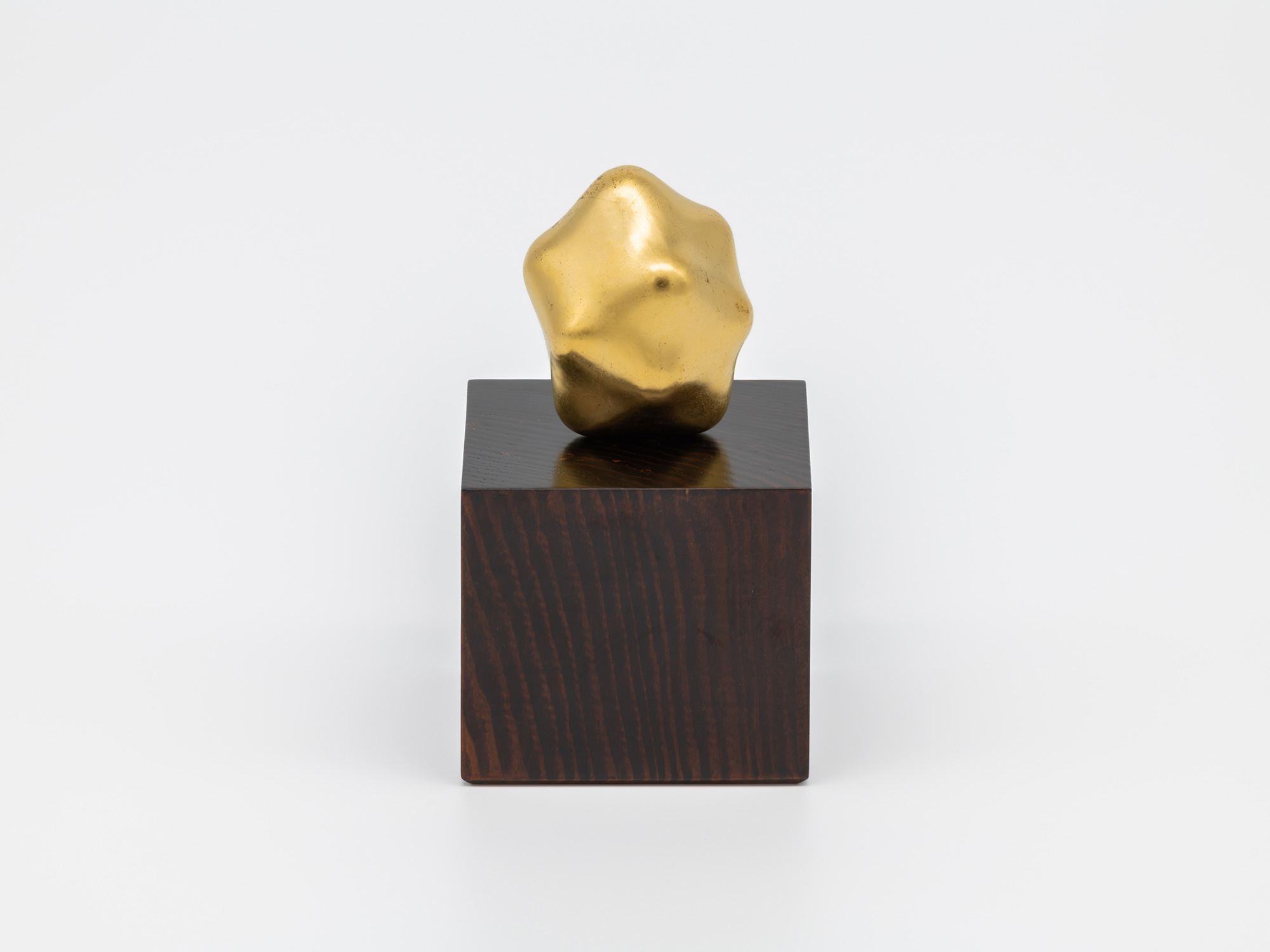 Untitled by Genta Ishizuka displayed with its accompanying wooden pedestal. A small, irregularly...
