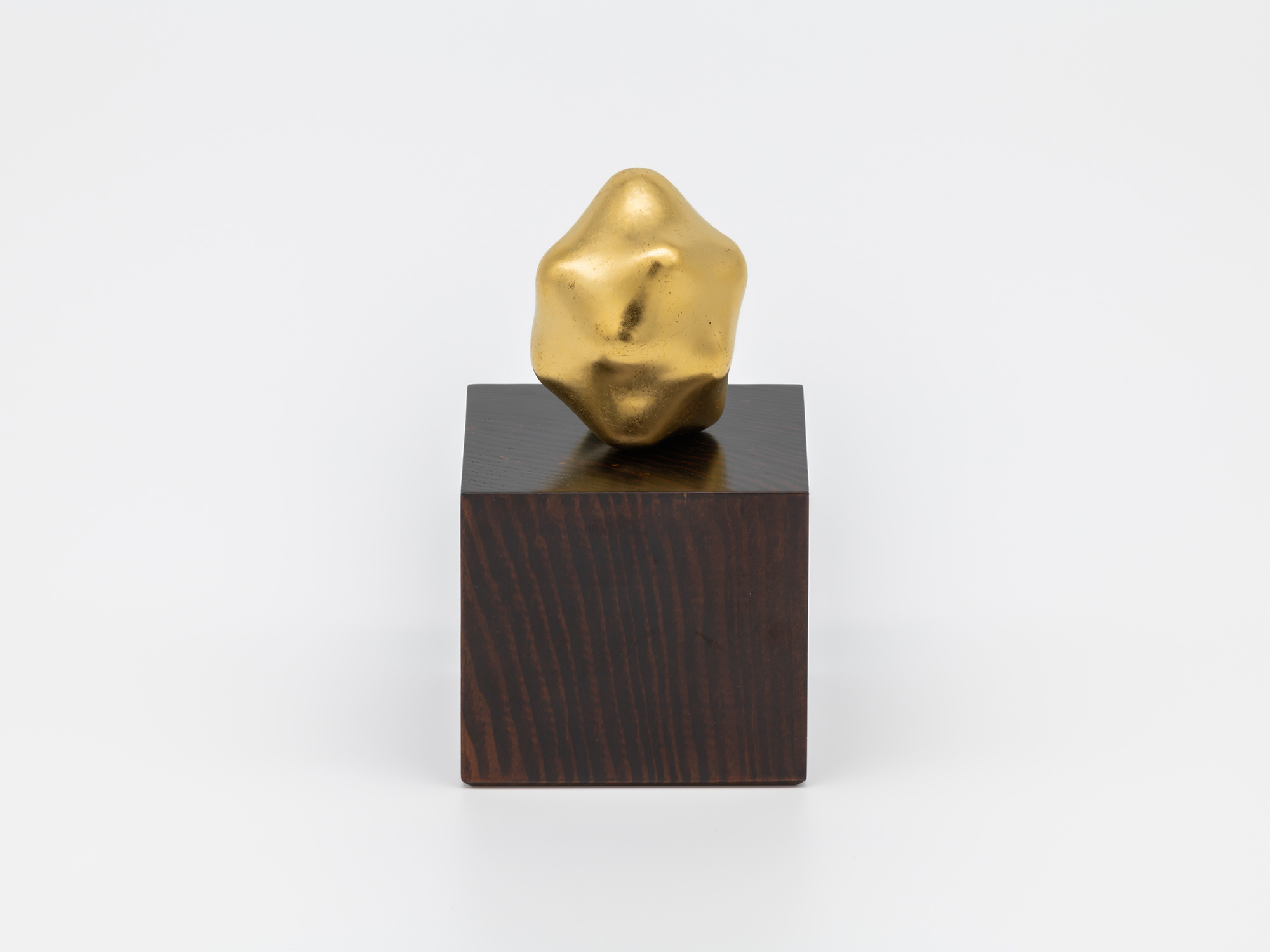 Untitled by Genta Ishizuka displayed with its accompanying wooden pedestal. A small, irregularly...