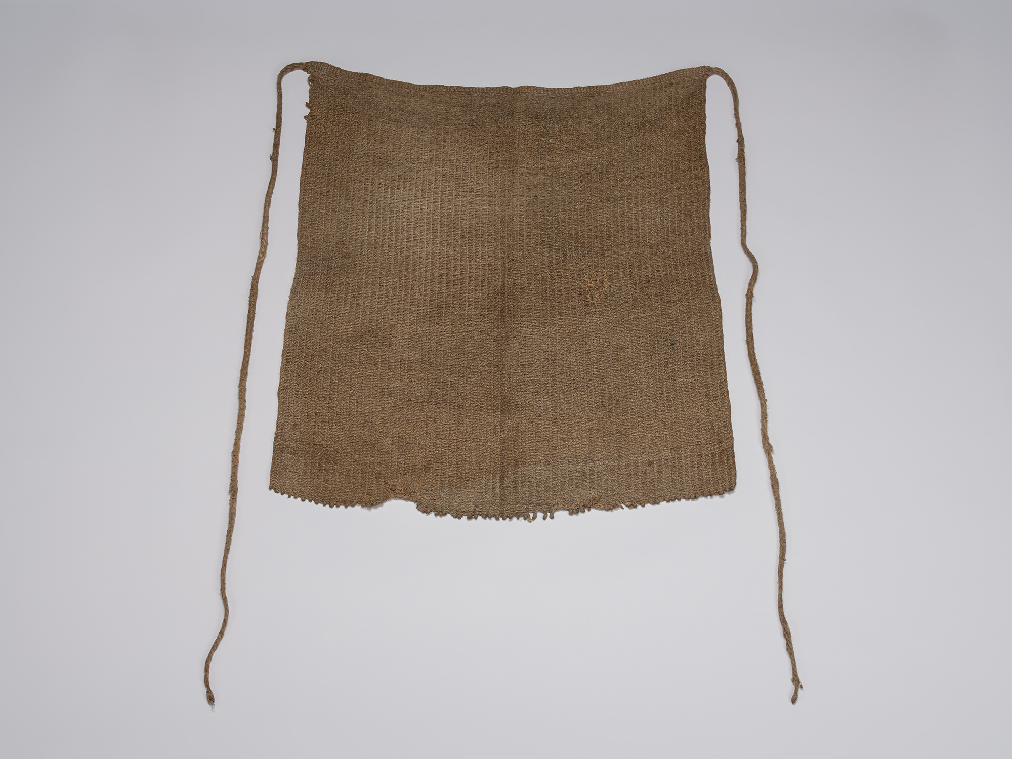 Full view of an angin maekake apron woven from natural brown bast fiber, with a rectangular body,...