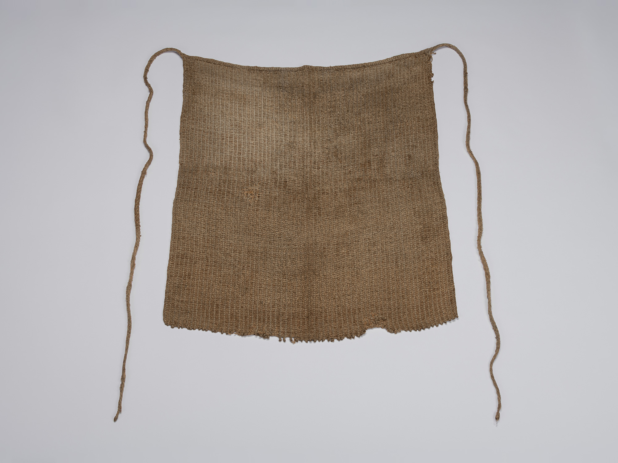 Full view of an angin maekake apron woven from natural brown bast fiber, with a rectangular body,...