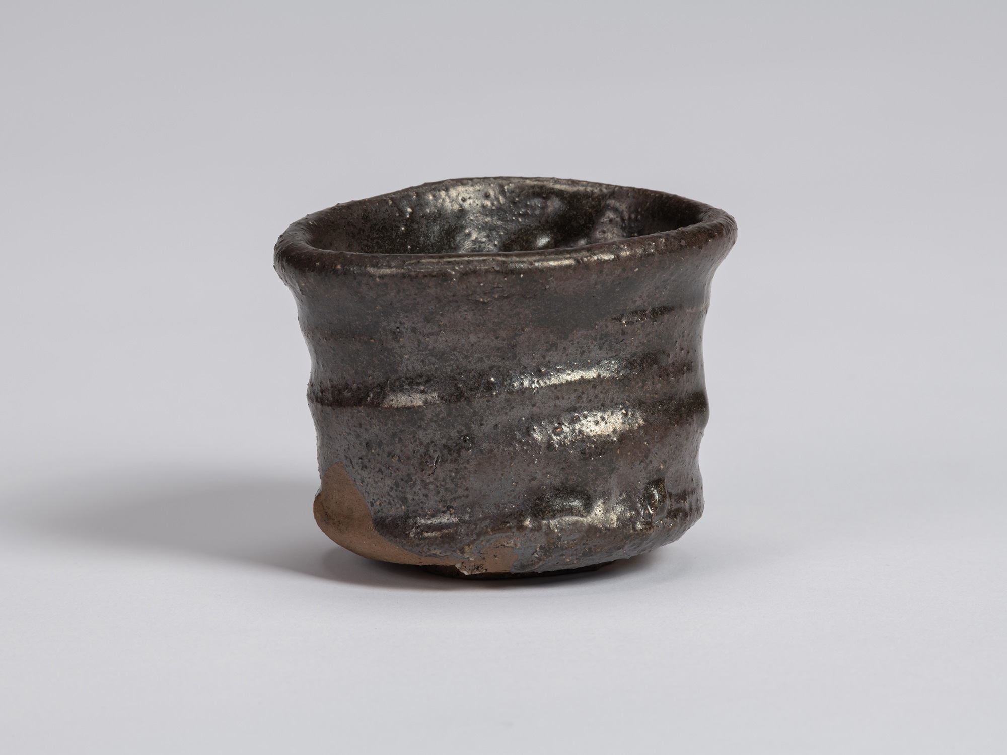 Kuro Guinomi by Shiro Tsujimura, with an irregular cylindrical form, dark black-brown glazed surface,...