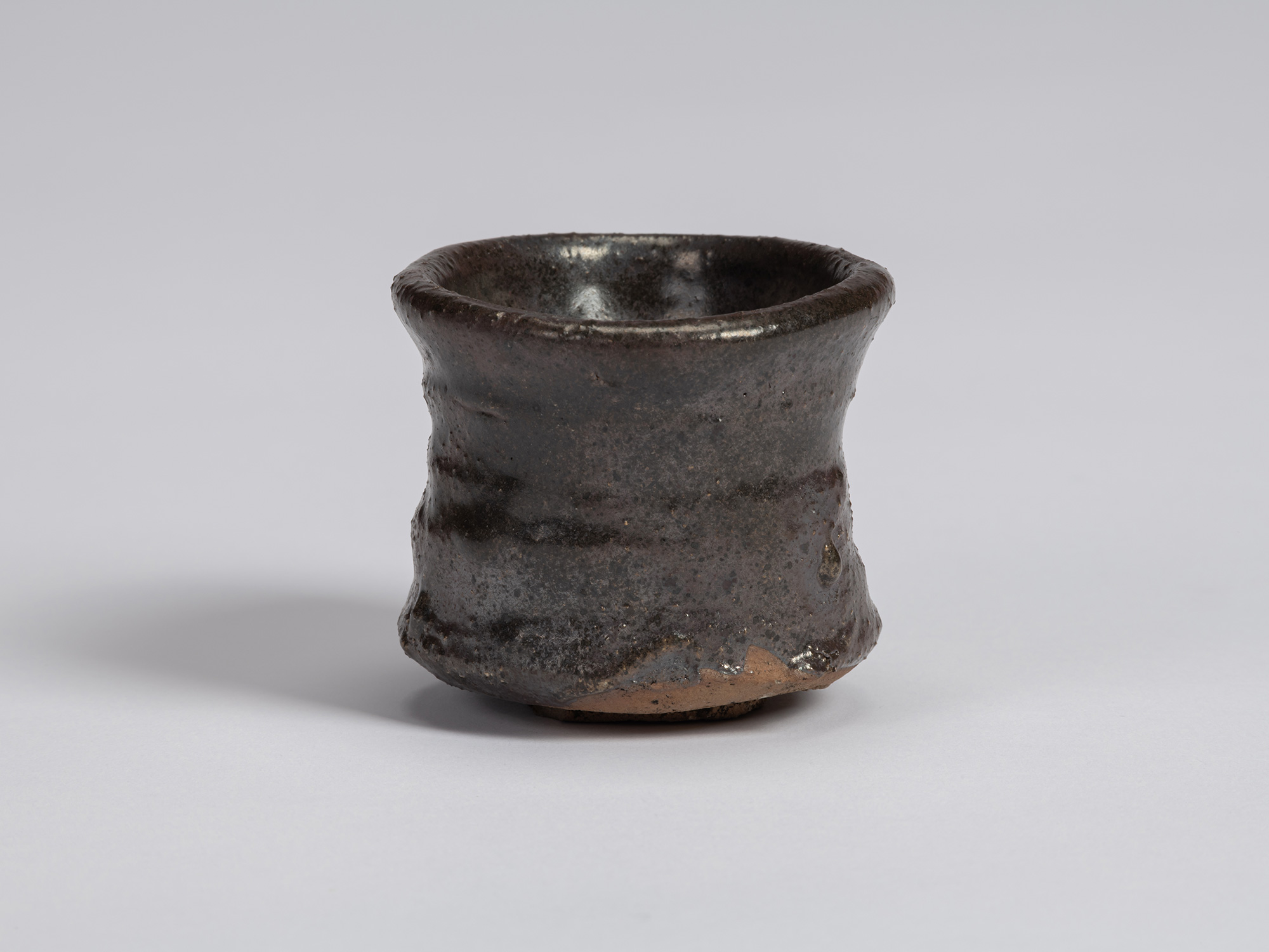 Kuro Guinomi by Shiro Tsujimura, with an irregular cylindrical form, dark black-brown glazed surface,...