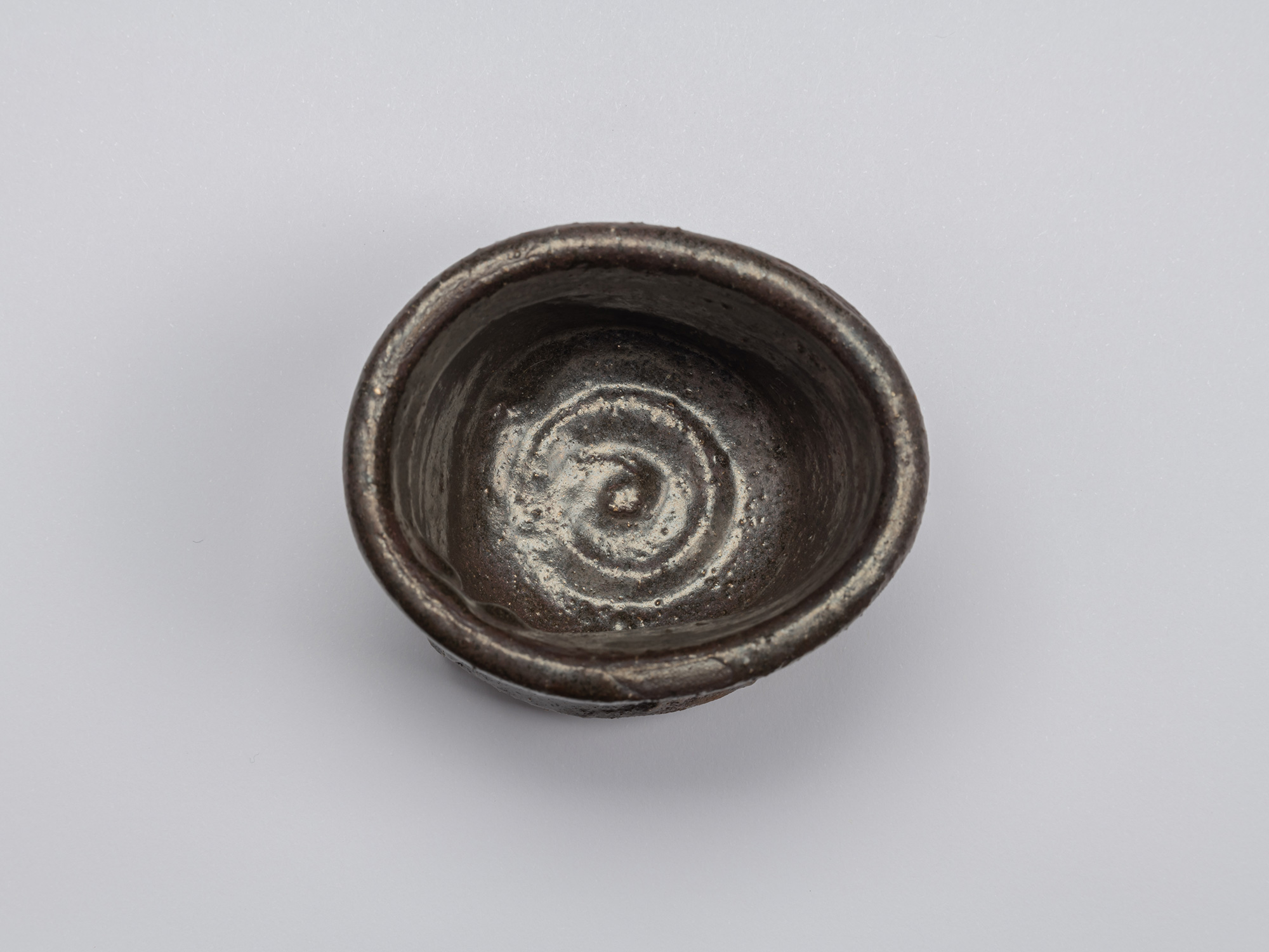 Interior of Shiro Tsujimura’s Kuro Guinomi, with a dark glossy glaze and prominent pale spiral...