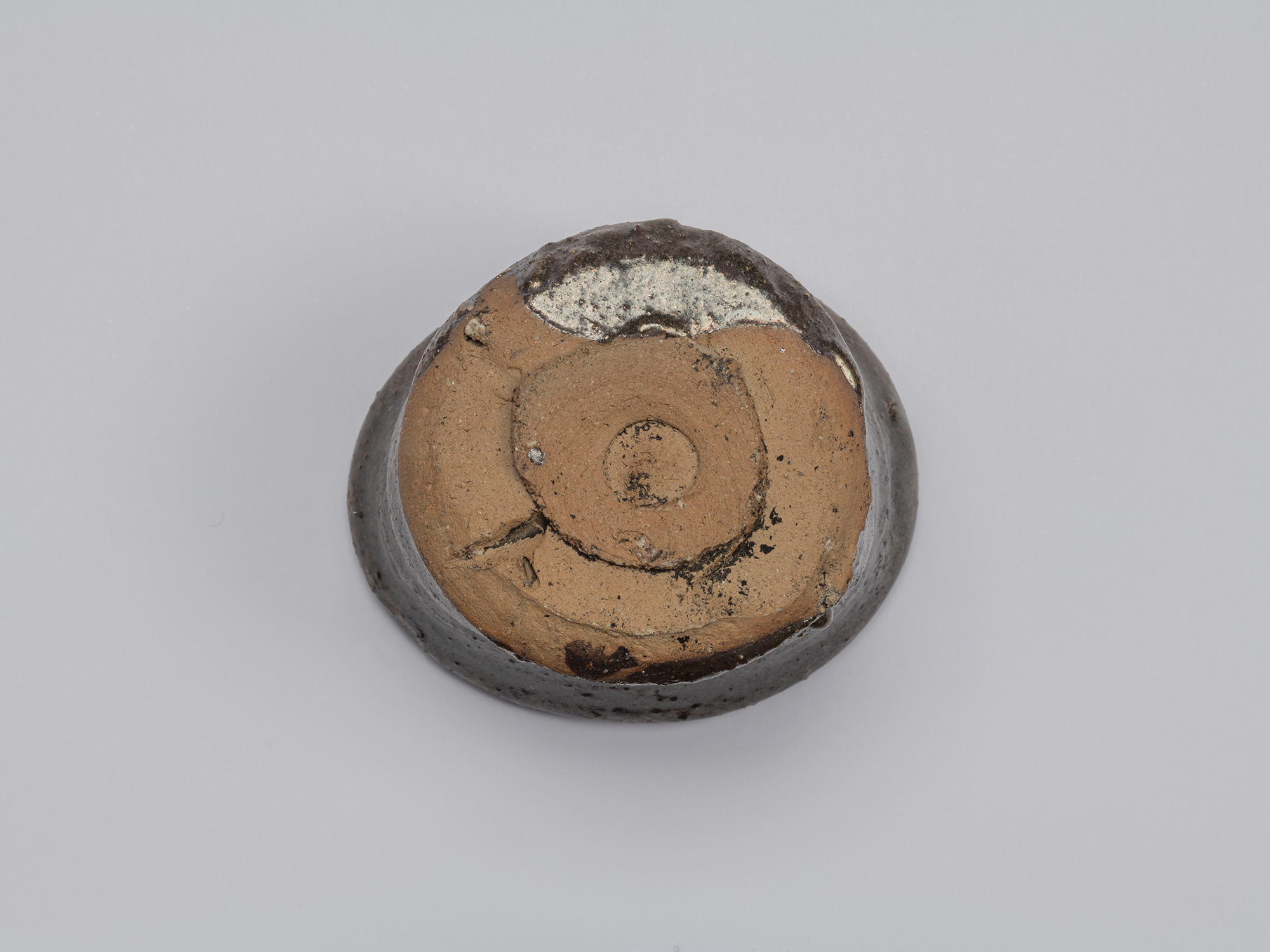 Underside of Shiro Tsujimura’s Kuro Guinomi, showing an unglazed clay base with a roughly formed...