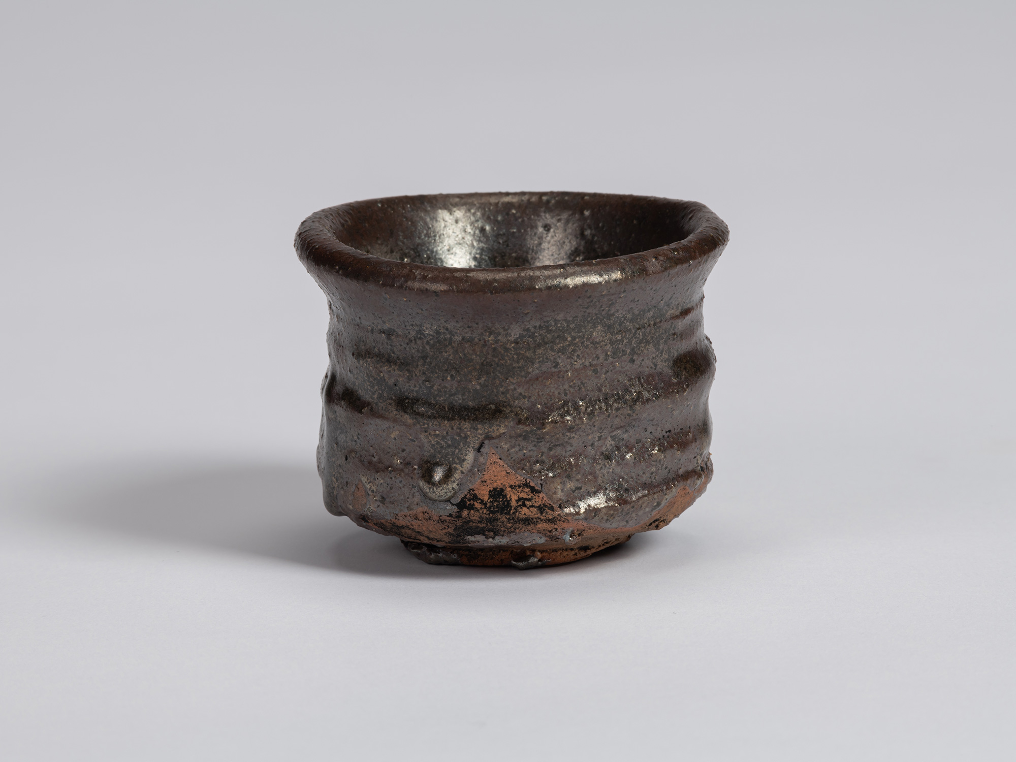 View of a Kuro Guinomi by Shiro Tsujimura, with a cylindrical form, slightly flared rim, and dark...