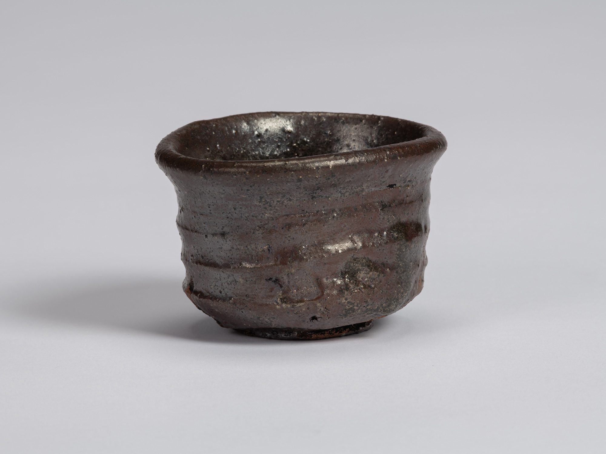 view of a Kuro Guinomi by Shiro Tsujimura, with a cylindrical form, slightly flared rim, and dark...