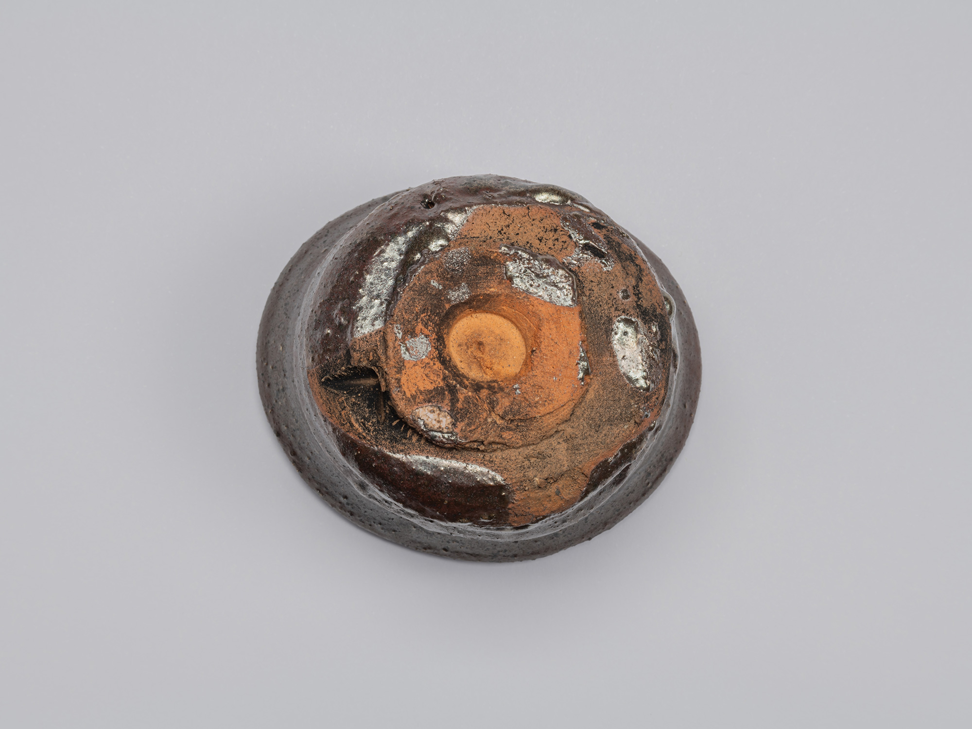Bottom view of the Kuro Guinomi, showing the roughly formed circular foot with exposed reddish-orange...