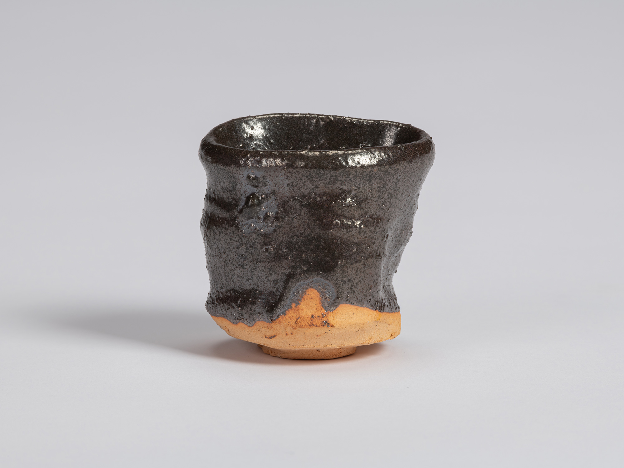 View of a Kuro Guinomi by Shiro Tsujimura, with a tall, slightly waisted cylindrical form, irregular...
