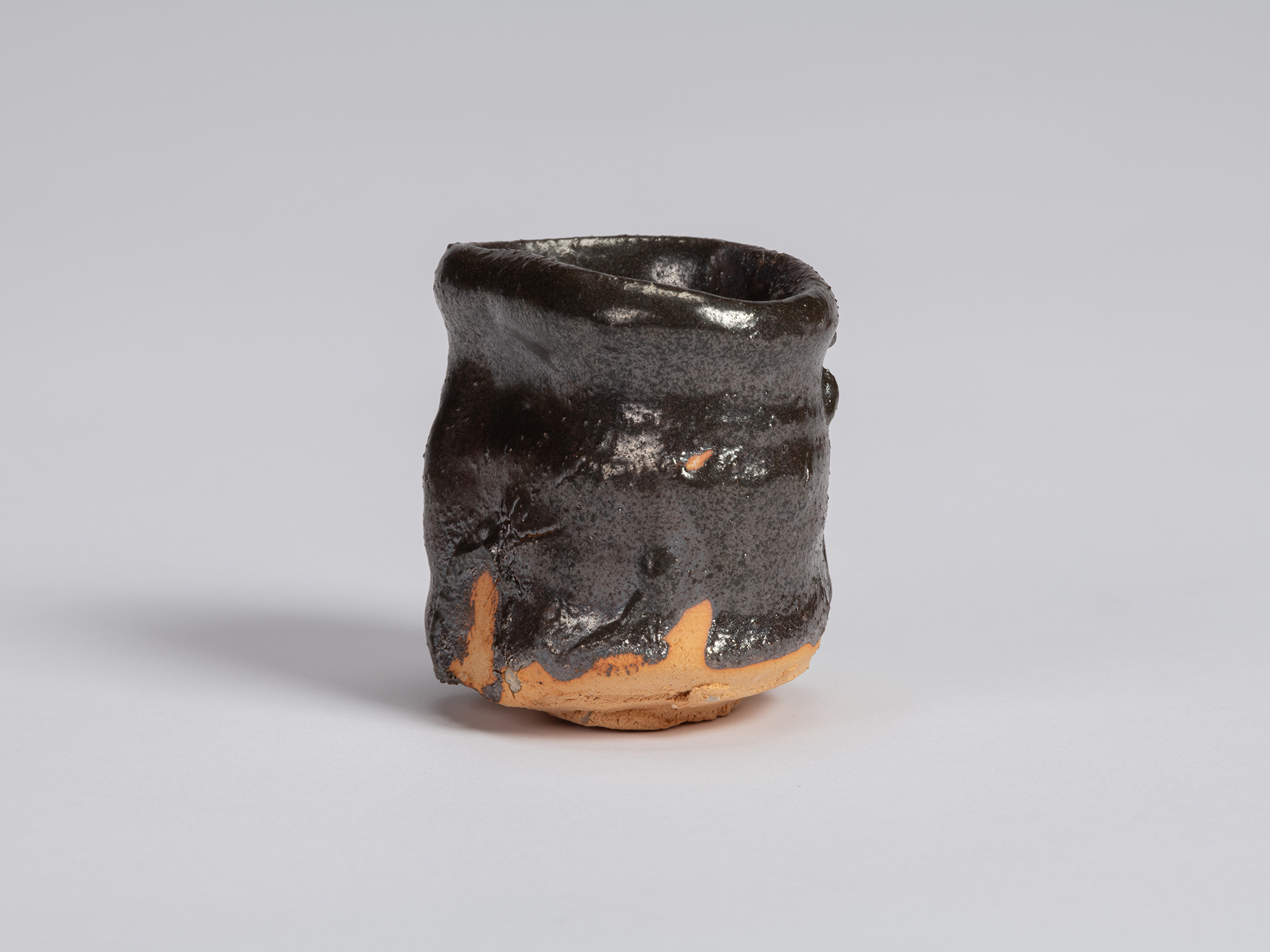 View of a Kuro Guinomi by Shiro Tsujimura, with a tall, slightly waisted cylindrical form, irregular...