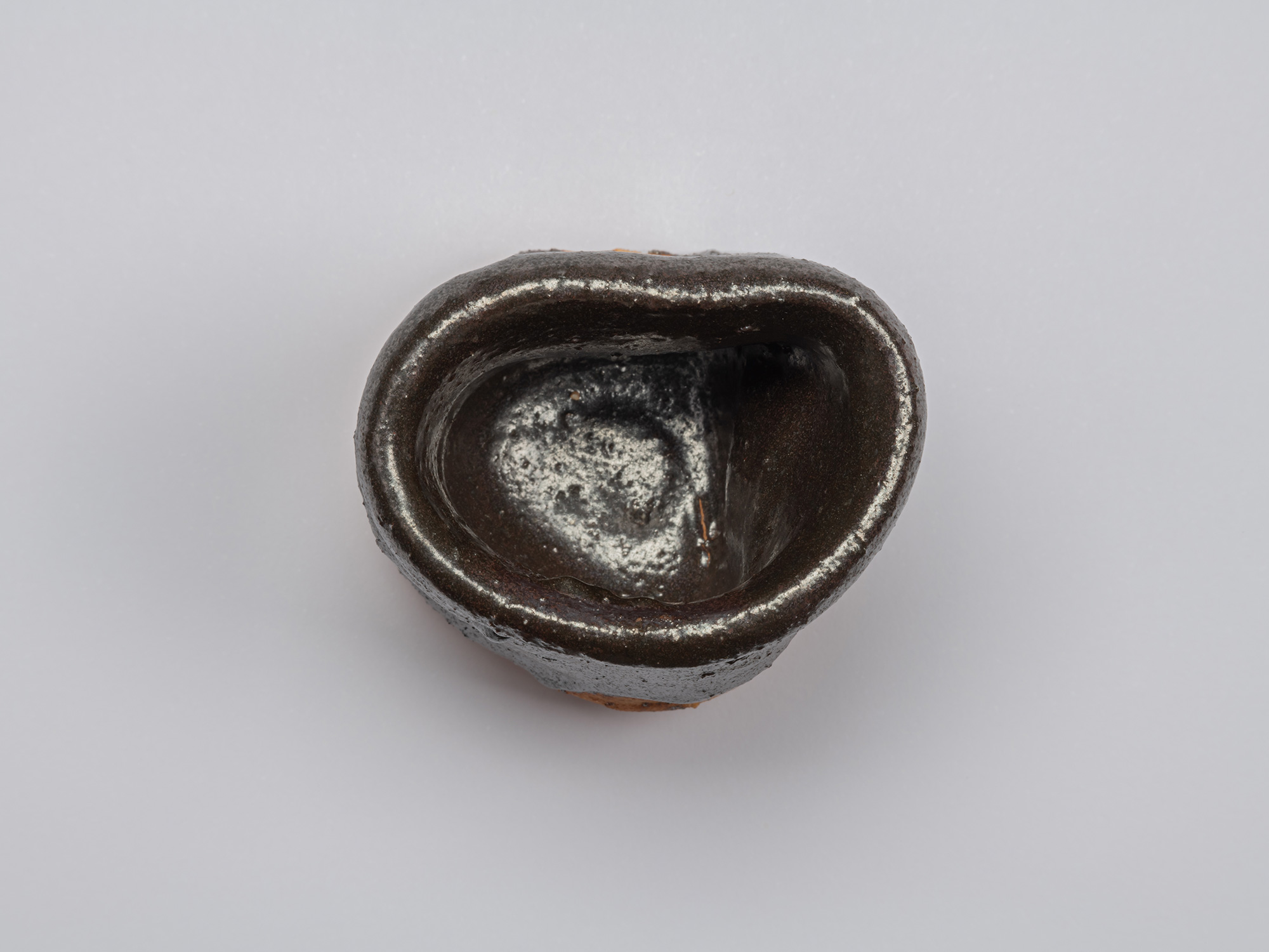 Overhead view of the Kuro Guinomi, showing its irregular, slightly squared rim and glossy dark...