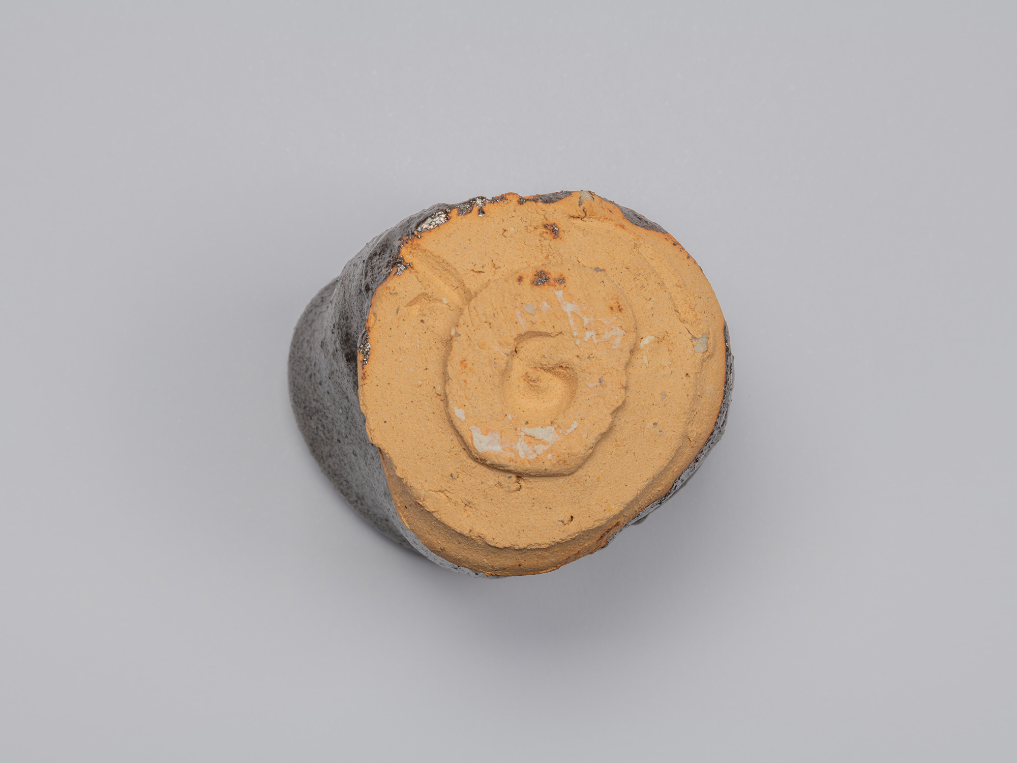 Bottom view of the Kuro Guinomi, showing the circular foot and largely unglazed orange clay base...