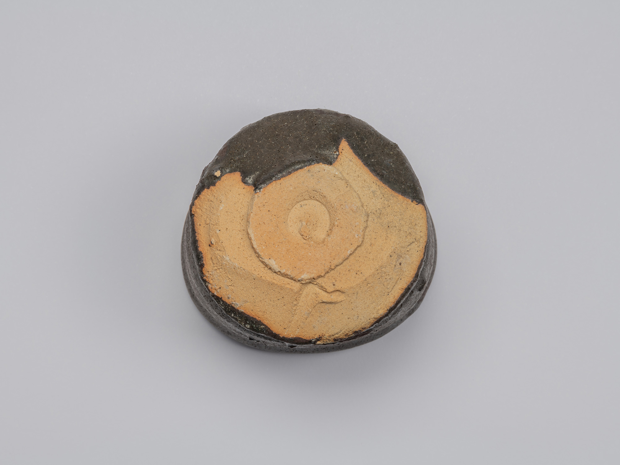 Bottom view of the Kuro Guinomi, showing a circular foot and broad area of exposed orange-buff...