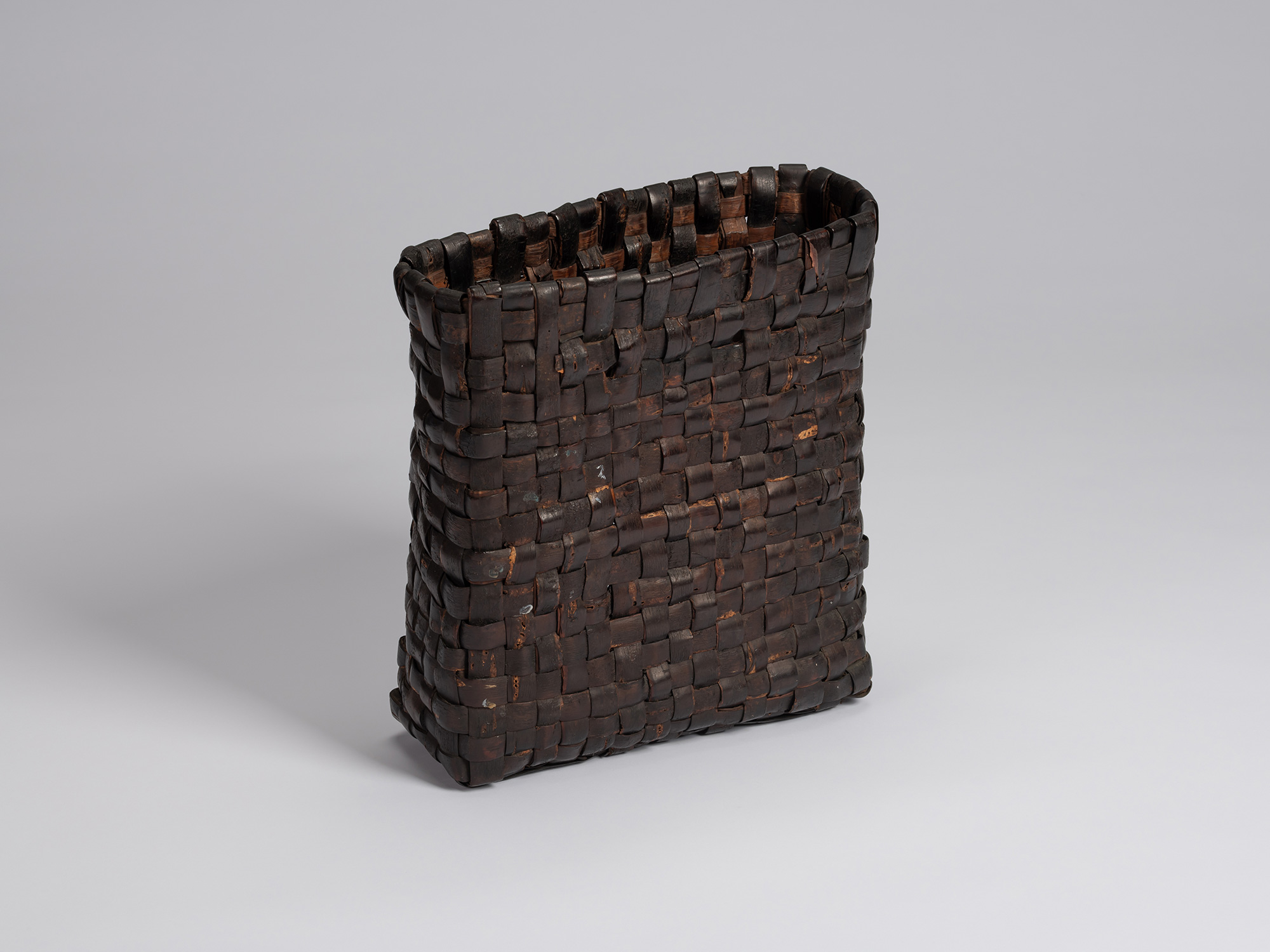 Three-quarter view of a rectangular kabakago basket woven with wild cherry bark, featuring a dark...