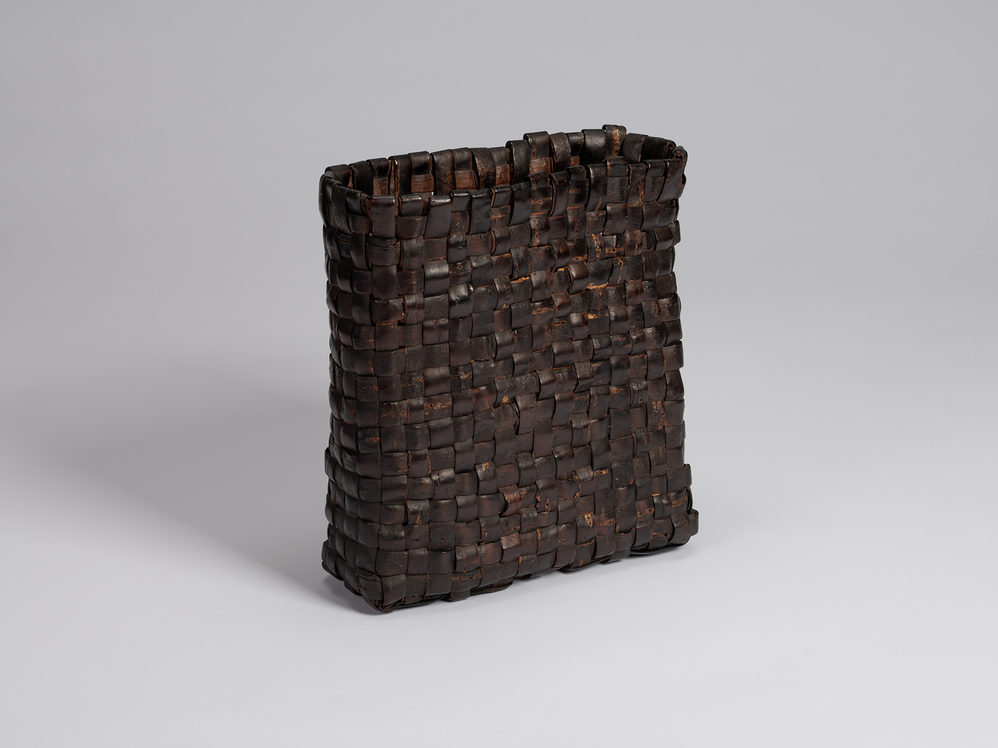Three-quarter view of a rectangular kabakago basket woven with wild cherry bark, featuring a dark...