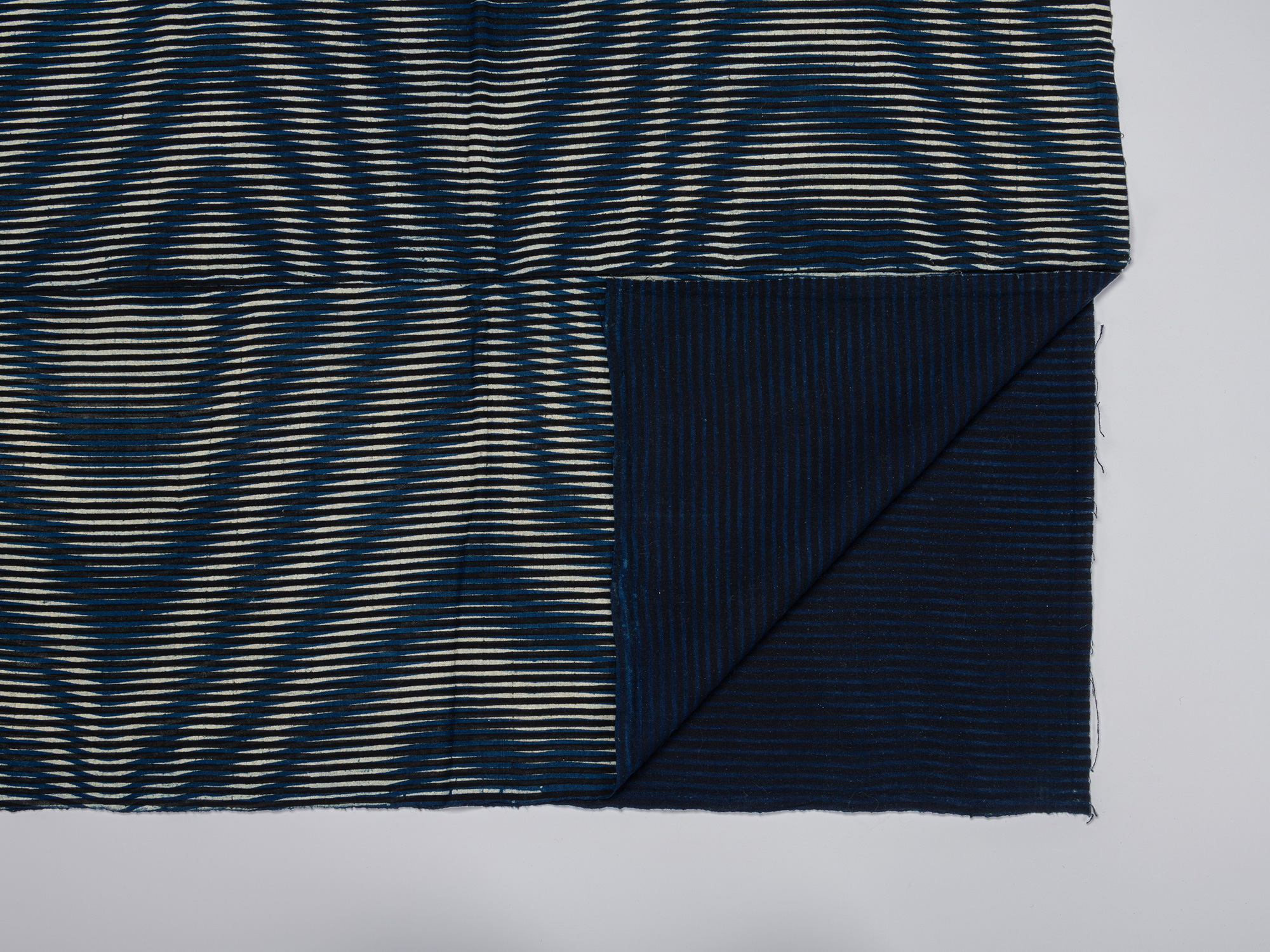 Detail of the kumanozome futon cover with one corner folded back, revealing the dark indigo reverse...
