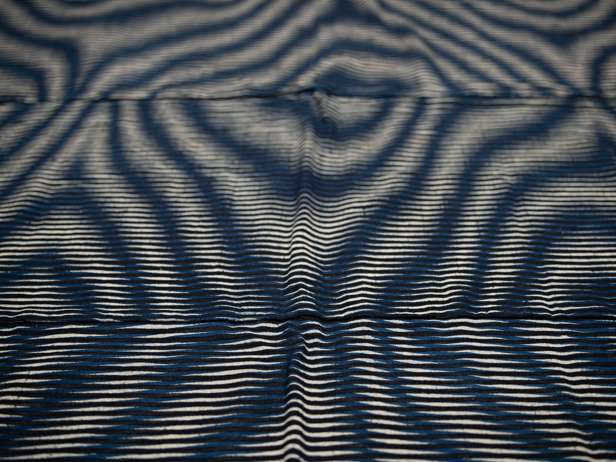 Detail view across the surface of the kumanozome futon cover, showing closely spaced indigo horizontal...