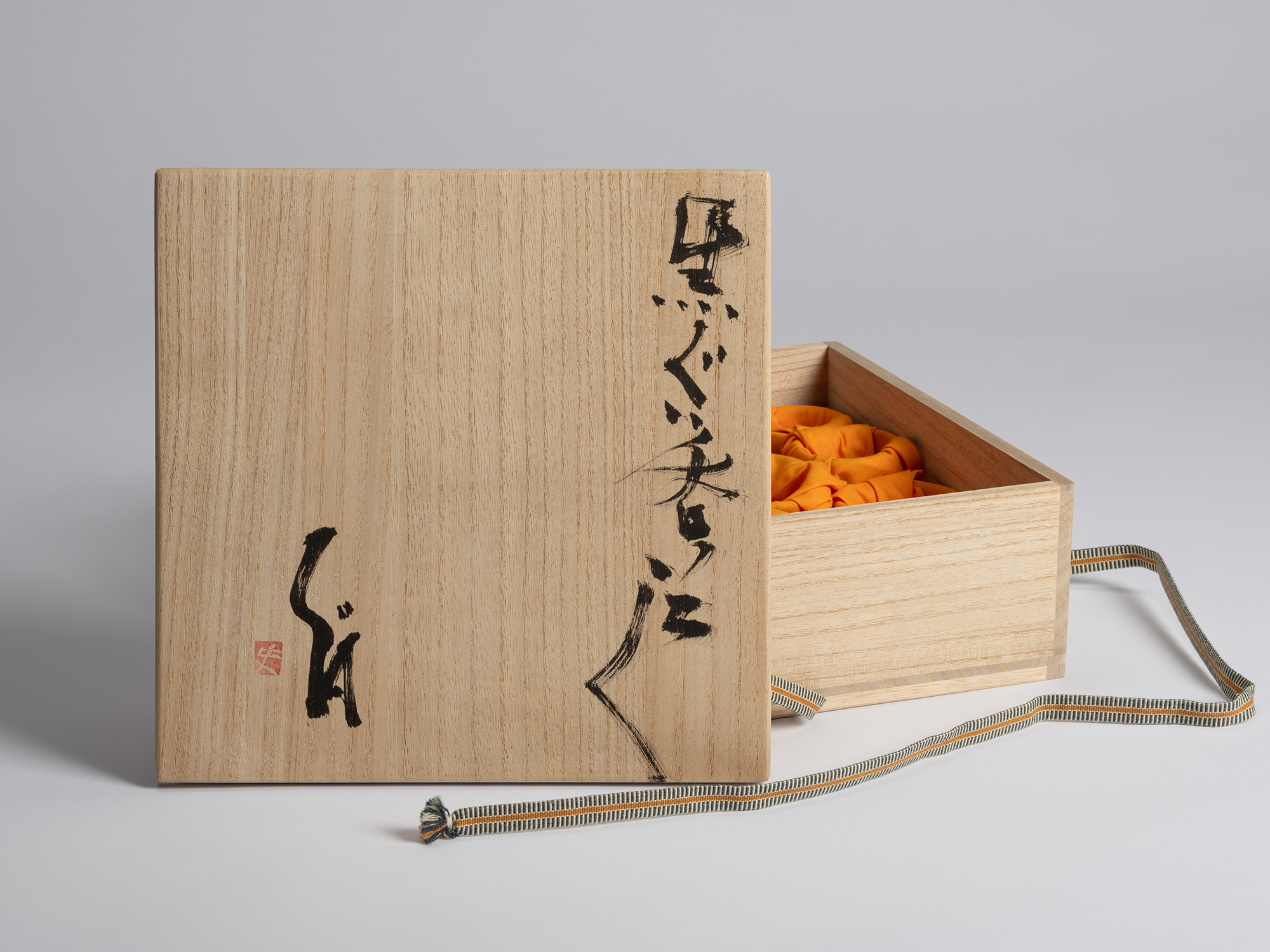 Open wooden tomobako for a set of ten Kuro Guinomi by Shiro Tsujimura, with the calligraphic lid...