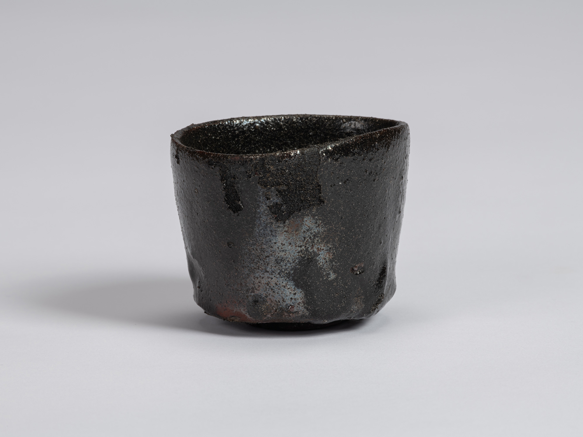 View of a Kuro Guinomi by Shiro Tsujimura, with an irregular cylindrical form, uneven rim, and...