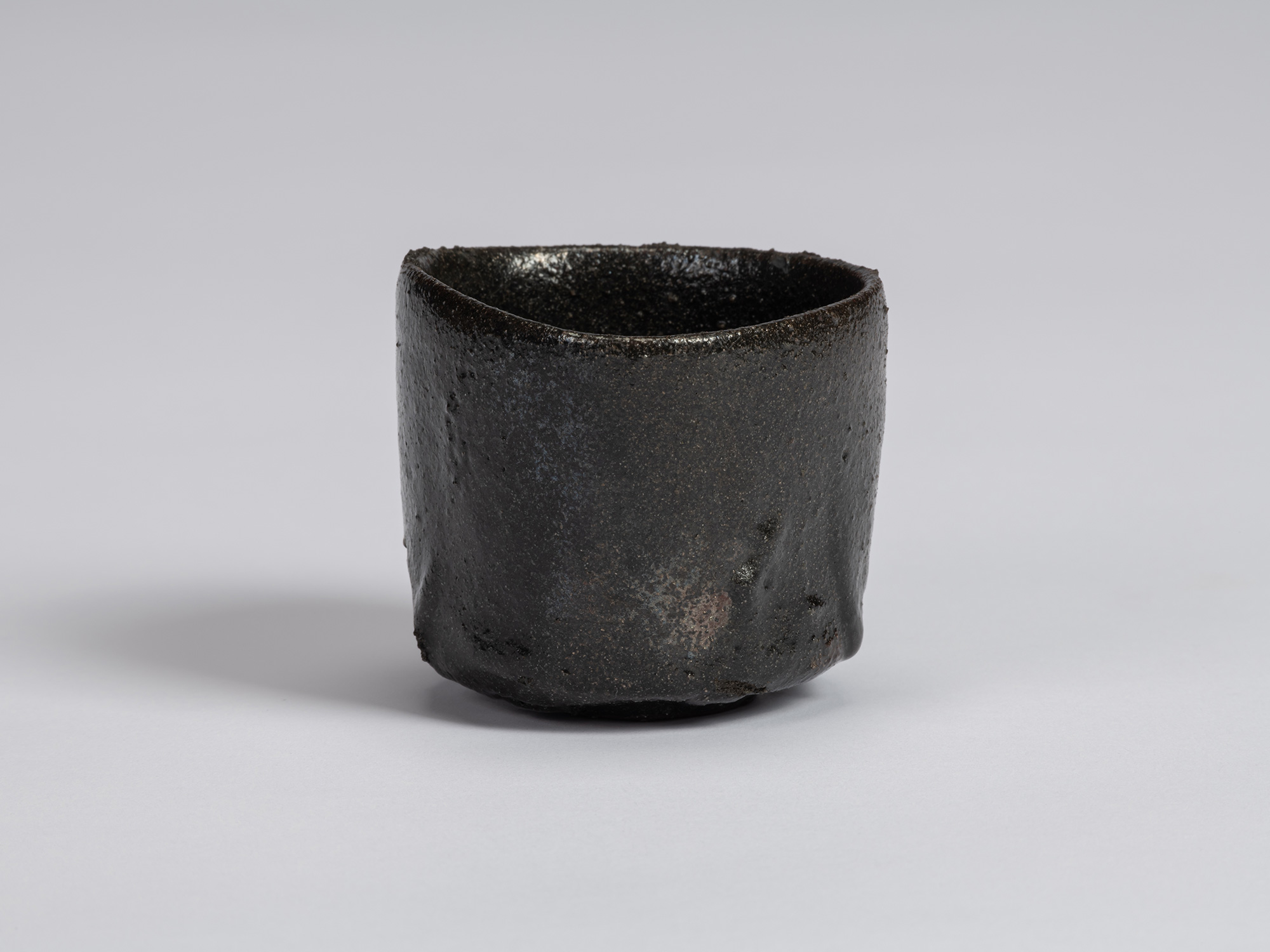 View of a Kuro Guinomi by Shiro Tsujimura, with an irregular cylindrical form, uneven rim, and...
