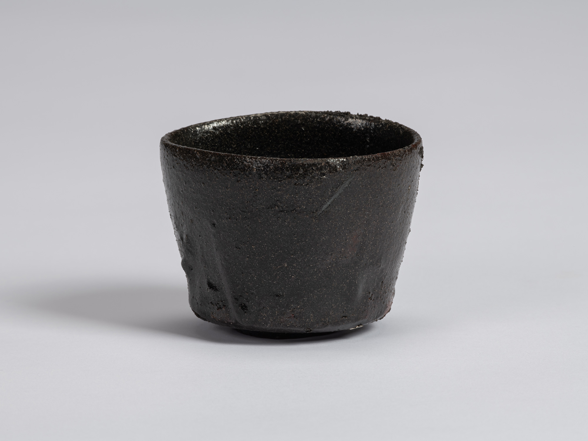 View of a Kuro Guinomi by Shiro Tsujimura, with an irregular cylindrical form, uneven rim, and...