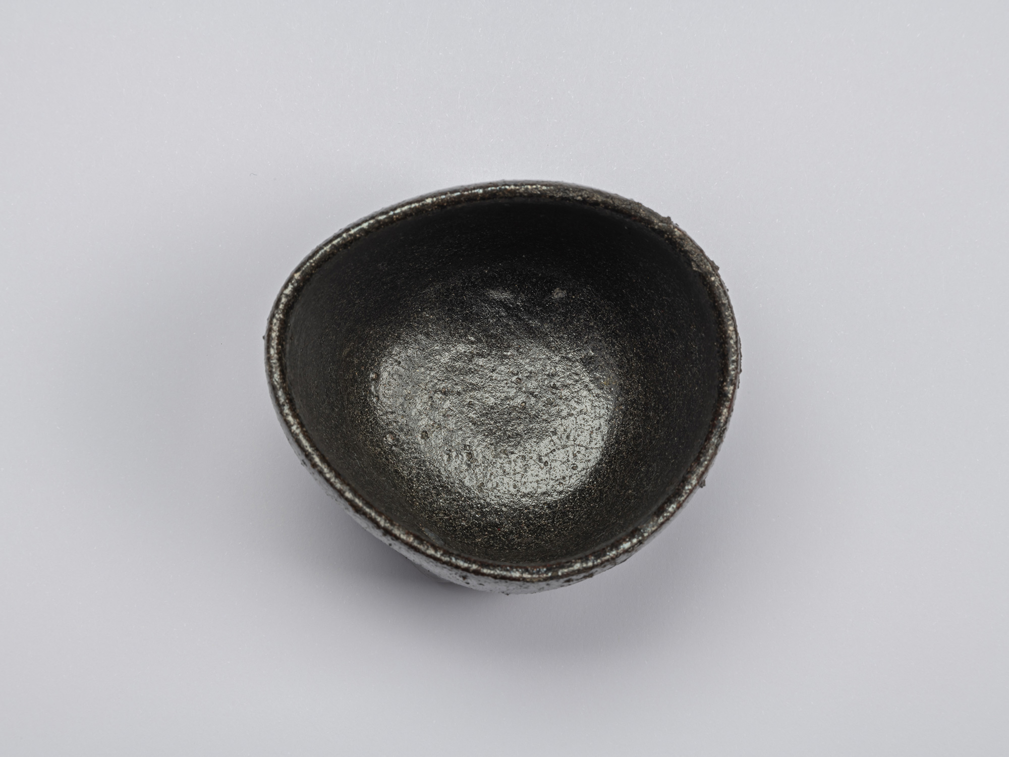 Overhead view of the Kuro Guinomi, showing its irregular rim and dark black-glazed interior with...