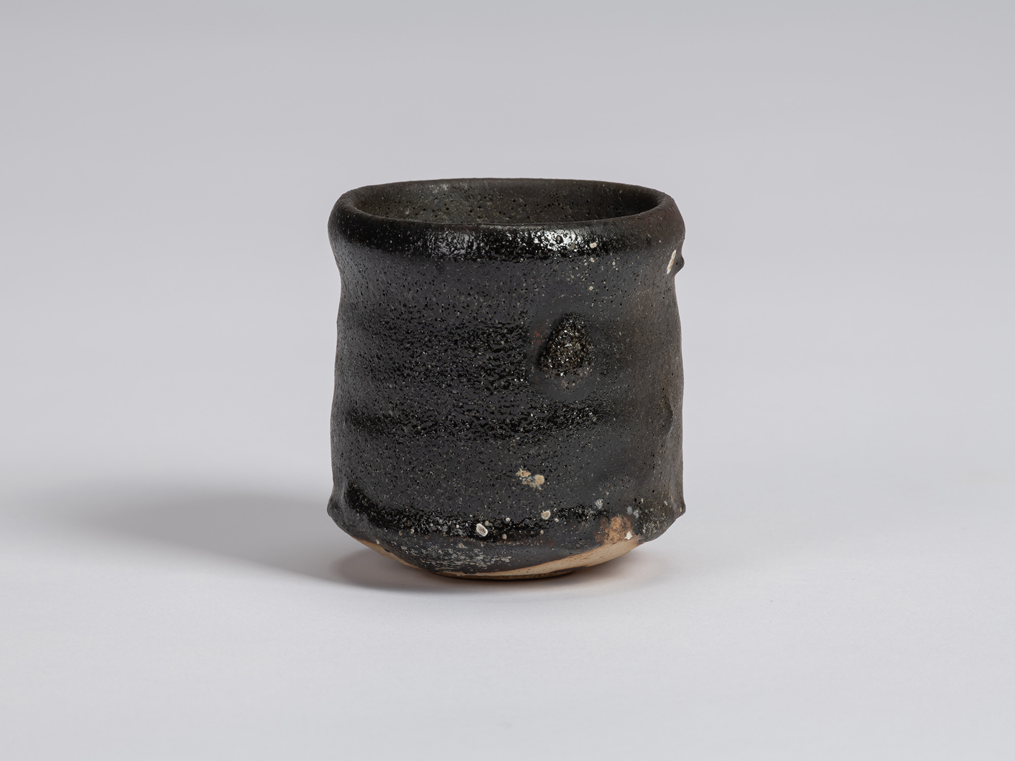 Kuro guinomi by Shiro Tsujimura with a tall, slightly irregular cylindrical form, rounded rim,...