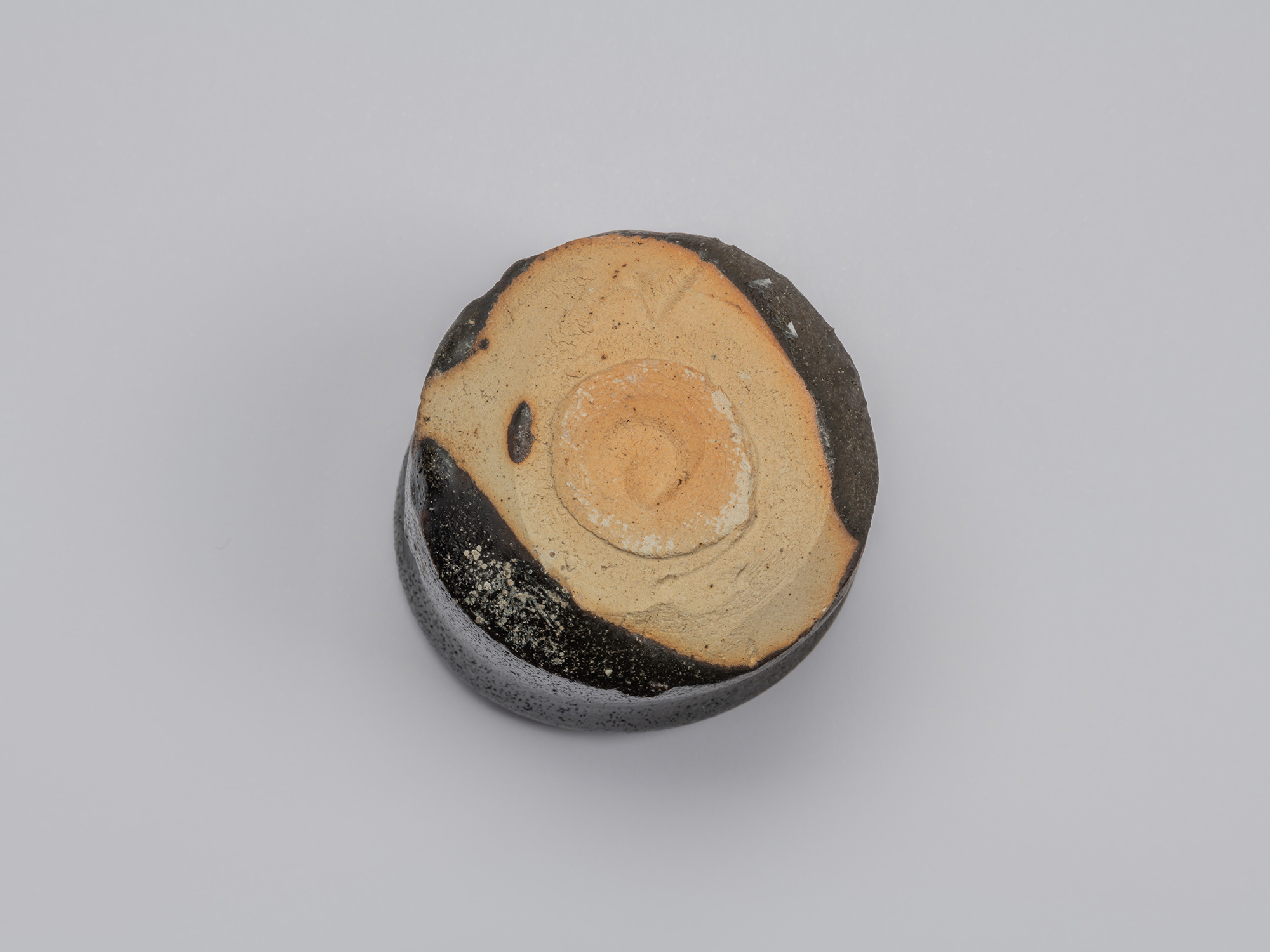 Underside of Shiro Tsujimura’s kuro guinomi showing a broad area of unglazed reddish-tan clay,...
