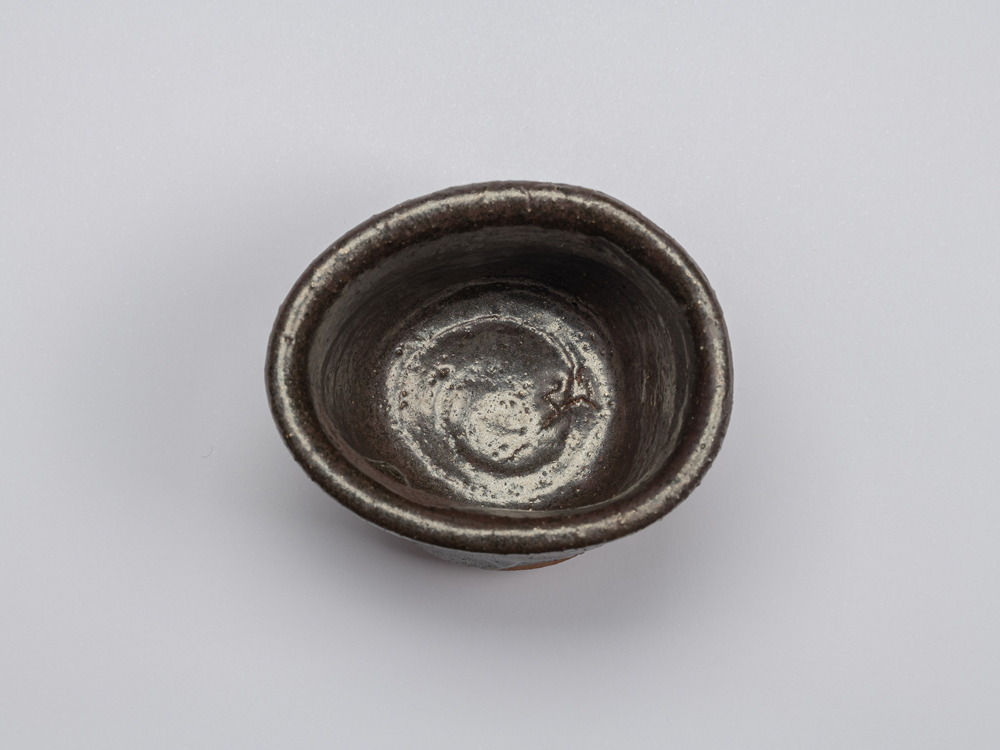 Overhead view of Shiro Tsujimura’s kuro guinomi showing an irregular rim and dark glazed interior...