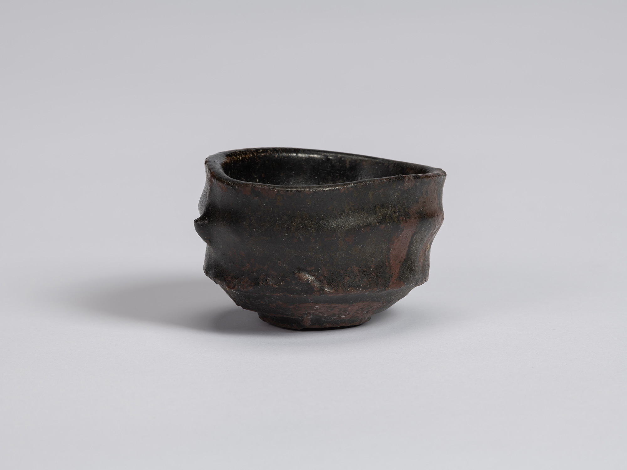 Kuro Guinomi by Shiro Tsujimura, with an irregular rounded form, undulating rim, and glossy black...