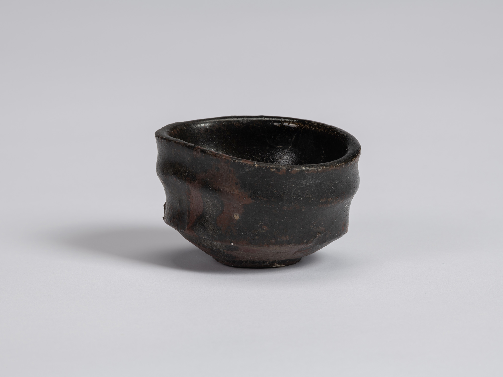 Kuro Guinomi by Shiro Tsujimura, with an irregular rounded form, undulating rim, and glossy black...