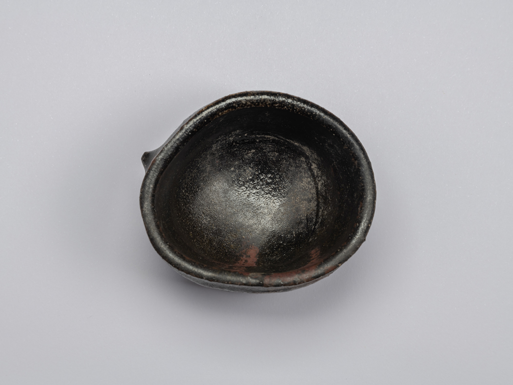 Interior of Shiro Tsujimura’s Kuro Guinomi, with a glossy black surface, subtle reddish-brown patches,...