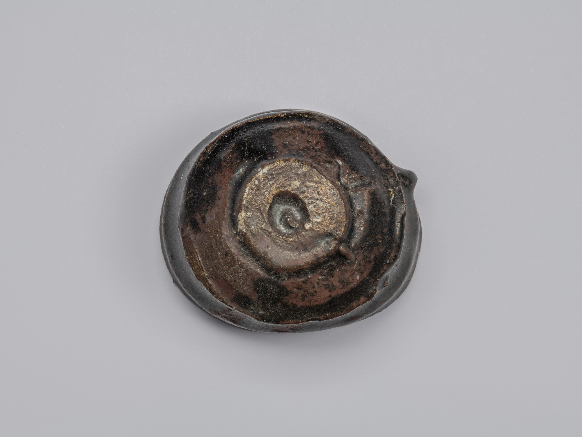 Underside of Shiro Tsujimura’s Kuro Guinomi, showing a roughly formed circular foot with black...