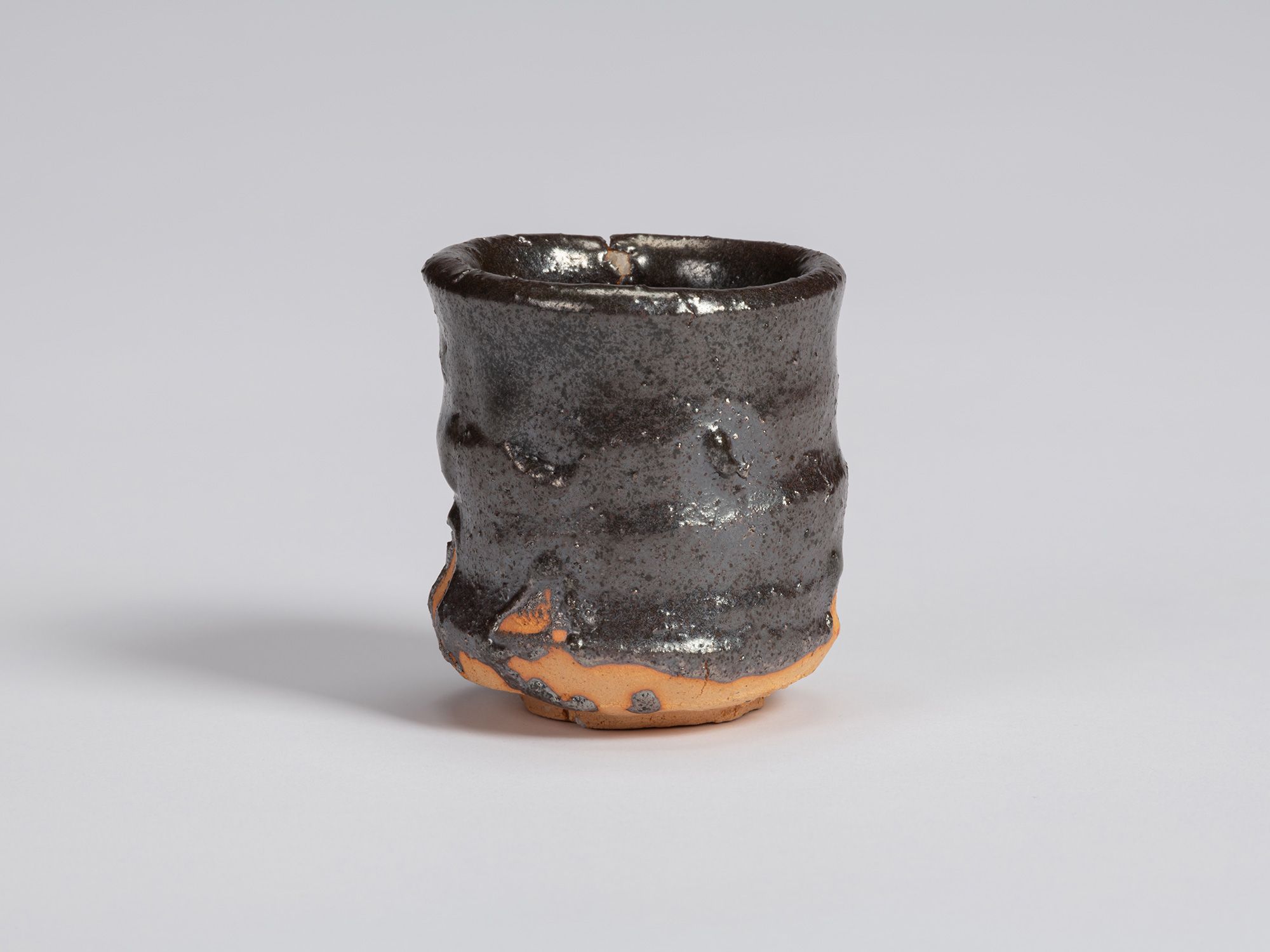 Kuro Guinomi by Shiro Tsujimura, with an irregular cylindrical form, glossy black glaze, and areas...