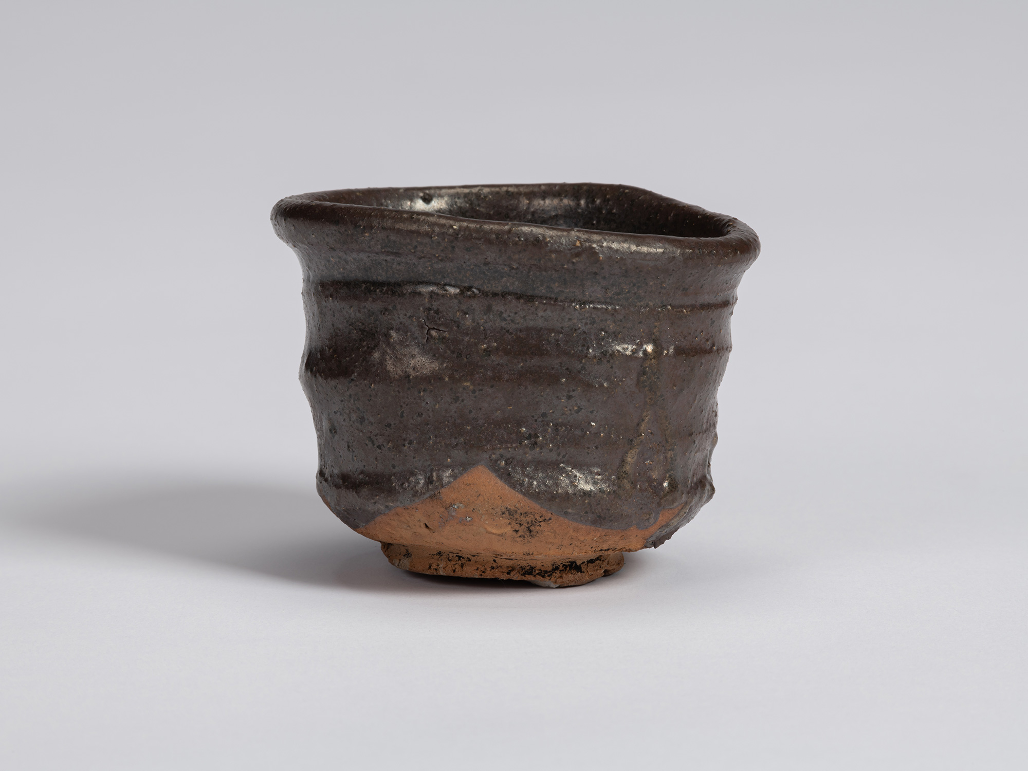 Kuro Guinomi by Shiro Tsujimura, with a broad, irregular cylindrical form, dark black-brown glaze,...