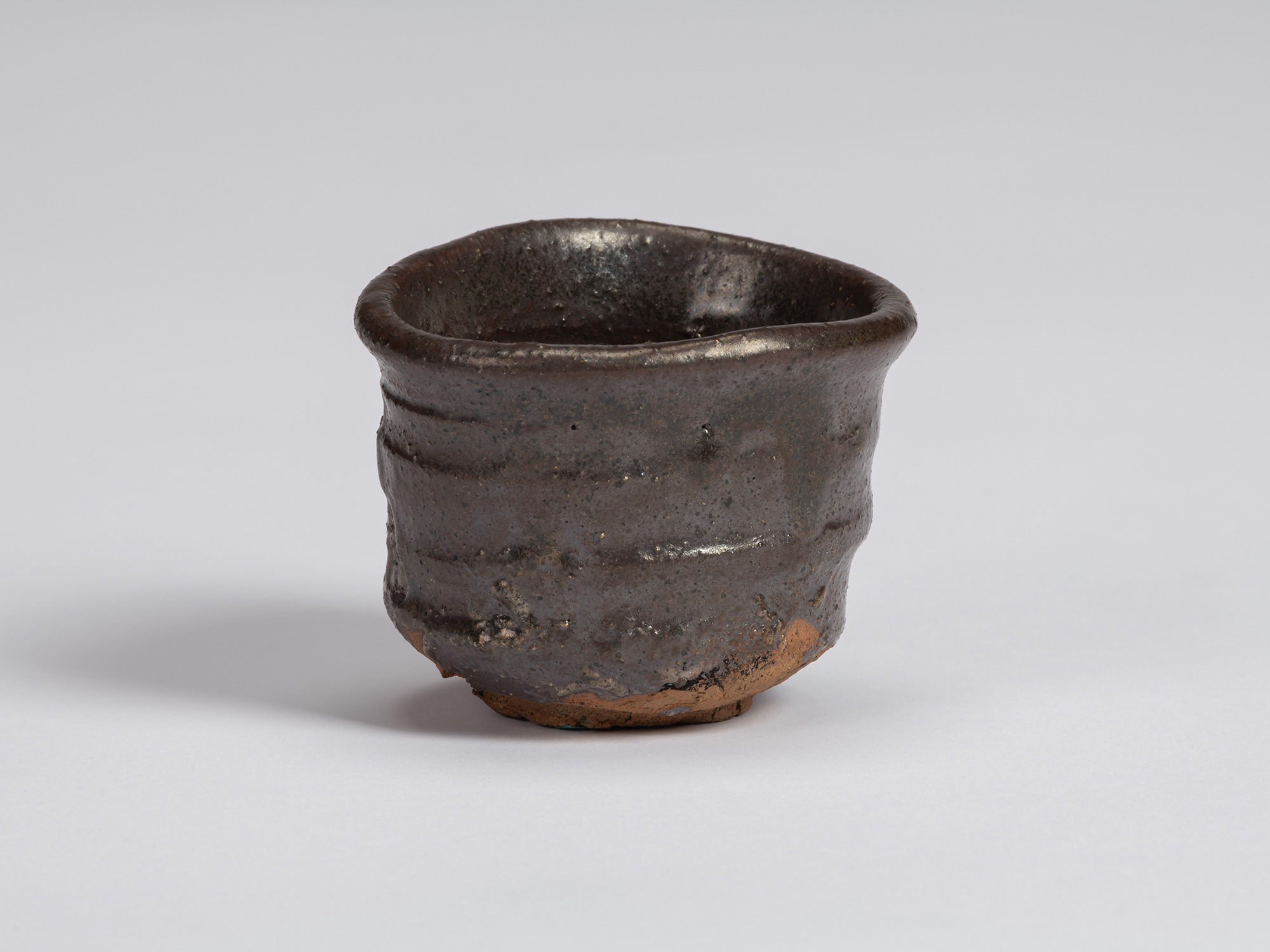 Kuro Guinomi by Shiro Tsujimura, with a broad, irregular cylindrical form, dark black-brown glaze,...