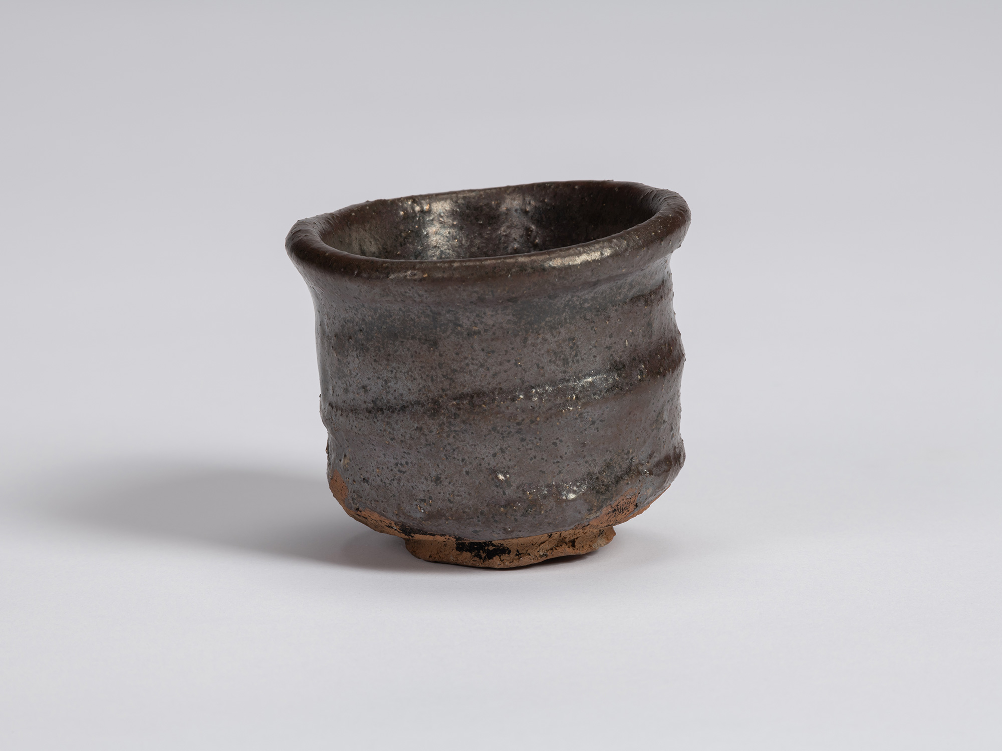 Kuro Guinomi by Shiro Tsujimura, with a broad, irregular cylindrical form, dark black-brown glaze,...