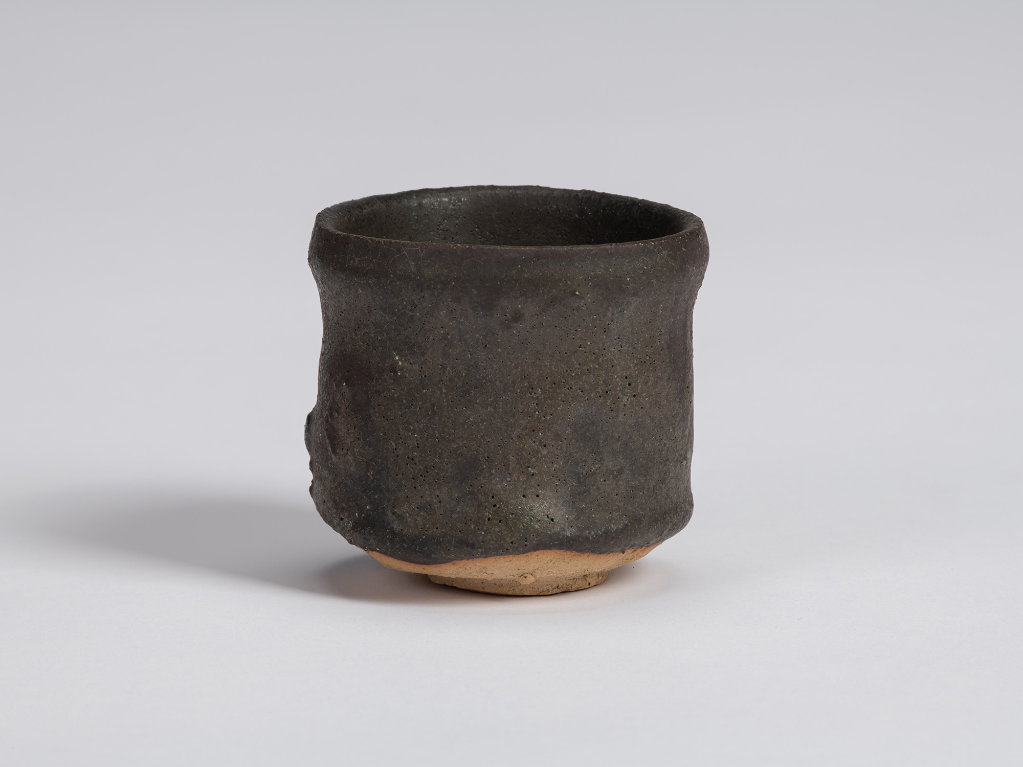 Kuro Guinomi by Shiro Tsujimura, with a tall cylindrical form, matte black-brown surface, subtly...