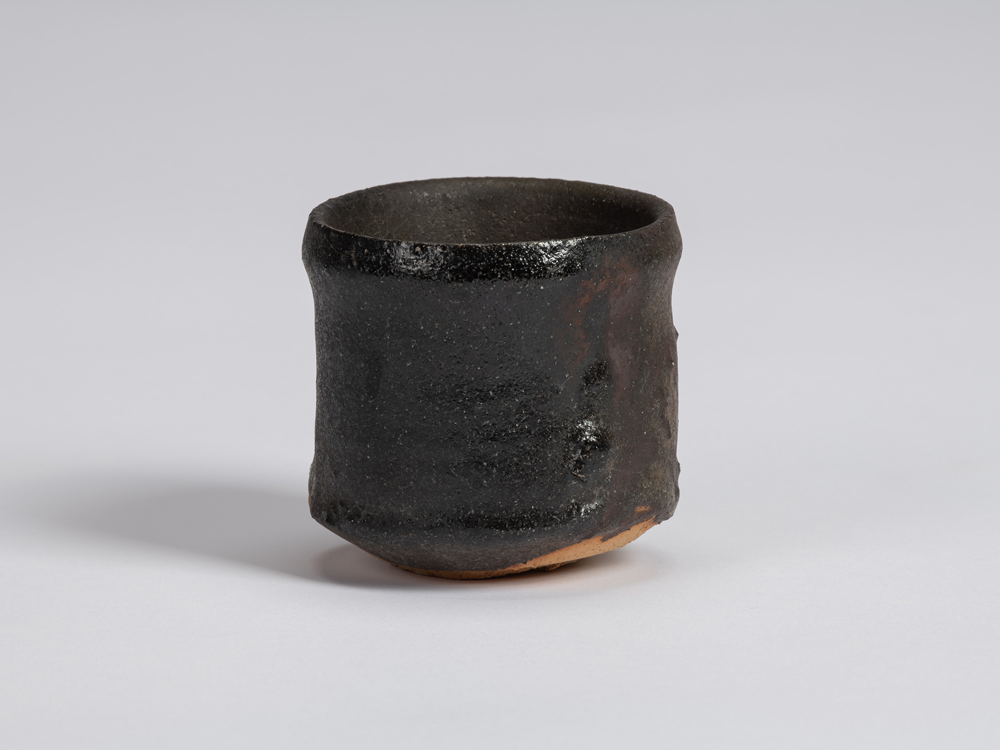 Kuro Guinomi by Shiro Tsujimura, with a tall cylindrical form, matte black-brown surface, subtly...