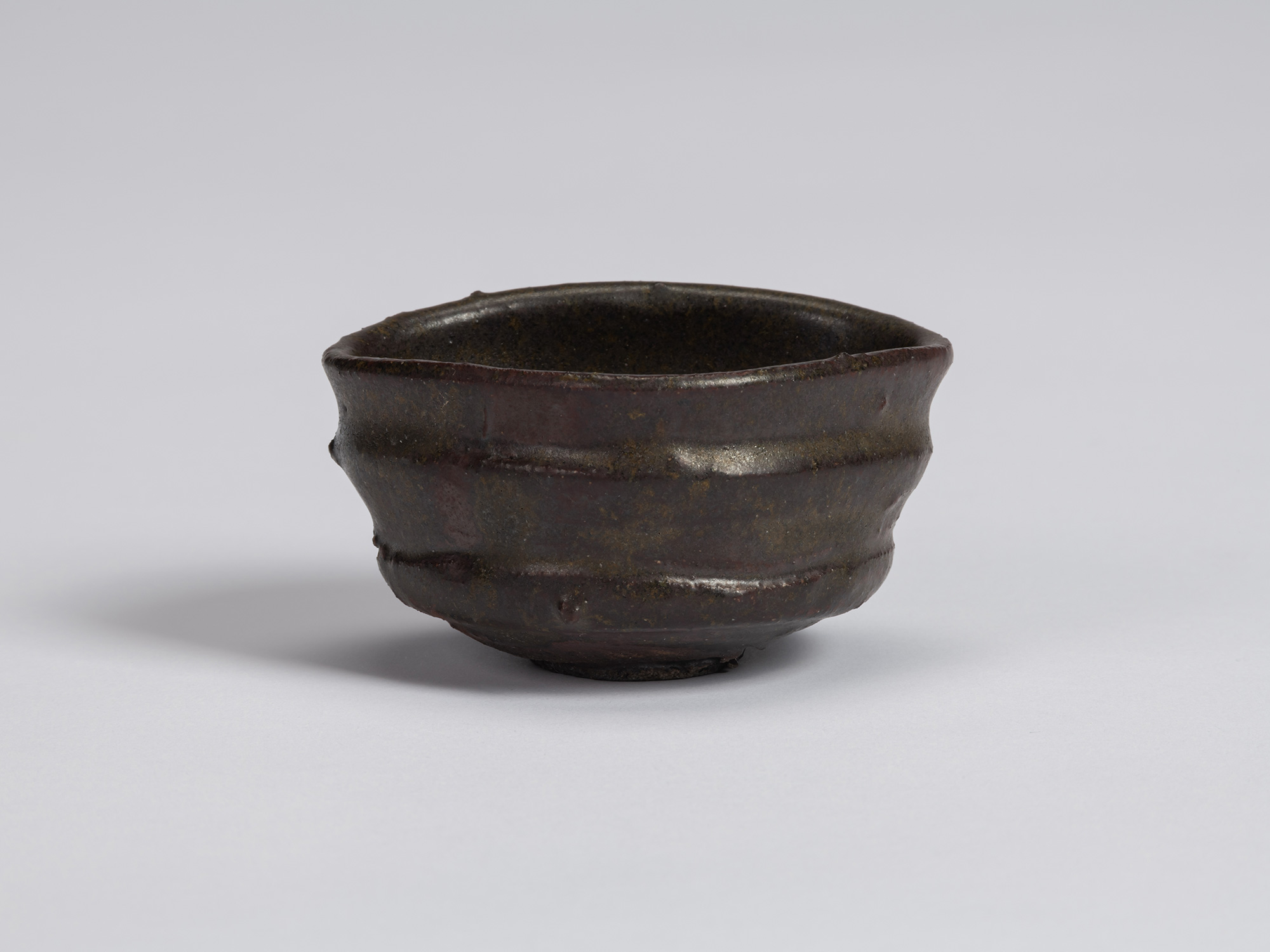 Kuro Guinomi by Shiro Tsujimura, with a low, broad form, dark black-brown glaze, irregular rim,...