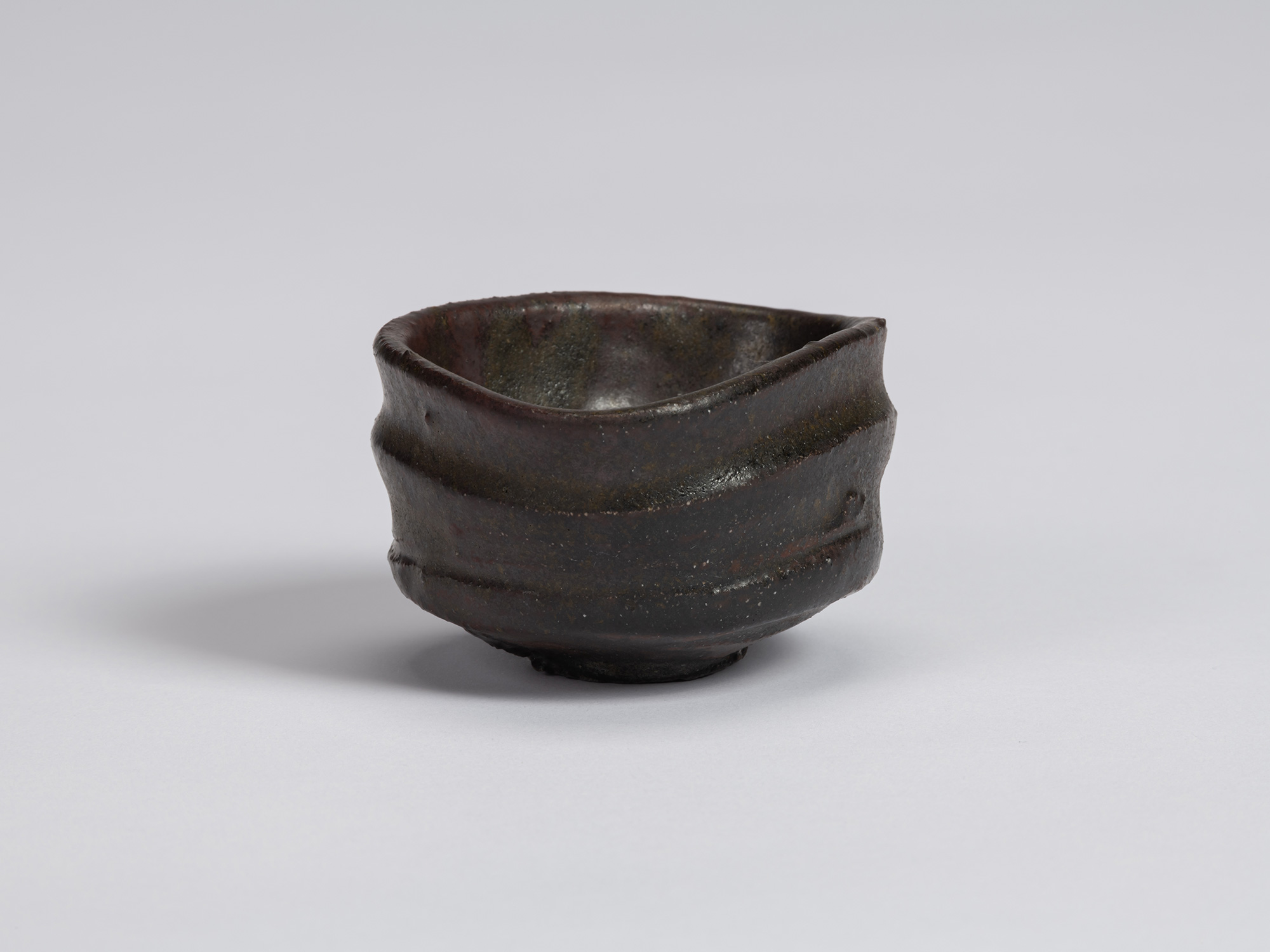 Kuro Guinomi by Shiro Tsujimura, with a low, broad form, dark black-brown glaze, irregular rim,...