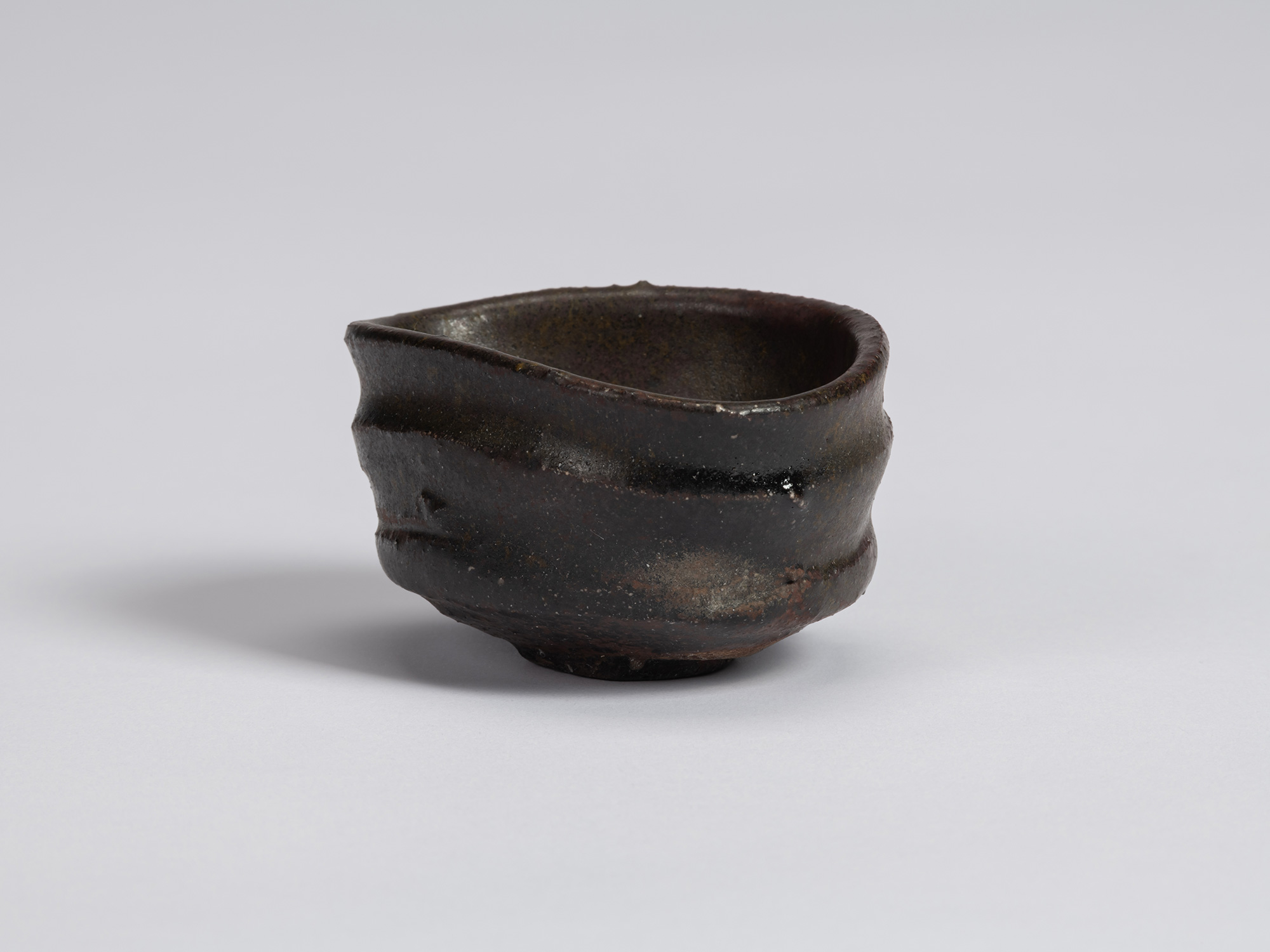 Kuro Guinomi by Shiro Tsujimura, with a low, broad form, dark black-brown glaze, irregular rim,...