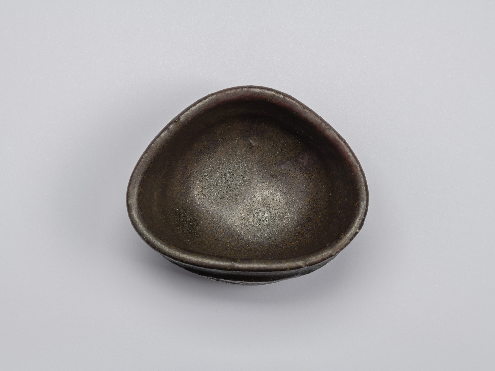 Aerial view of Kuro Guinomi by Shiro Tsujimura, showing an irregular oval rim and dark black-brown...