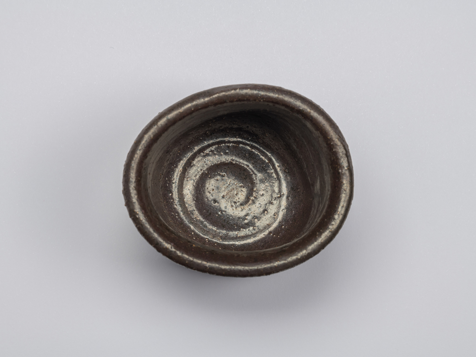 Overhead view of the Kuro Guinomi, showing the irregular rounded rim and dark glazed interior with...