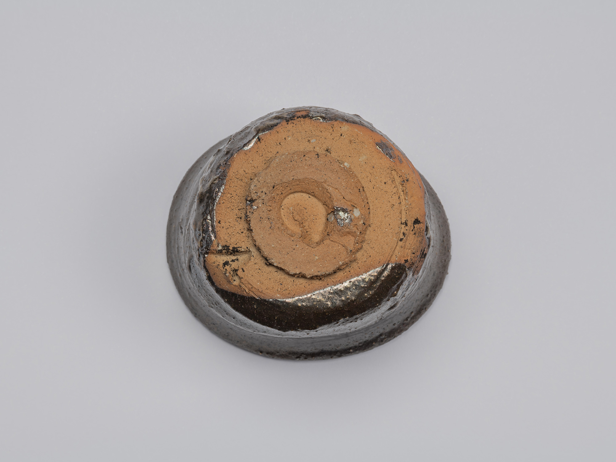 Bottom view of the Kuro Guinomi, showing a circular foot and largely unglazed orange-brown clay...
